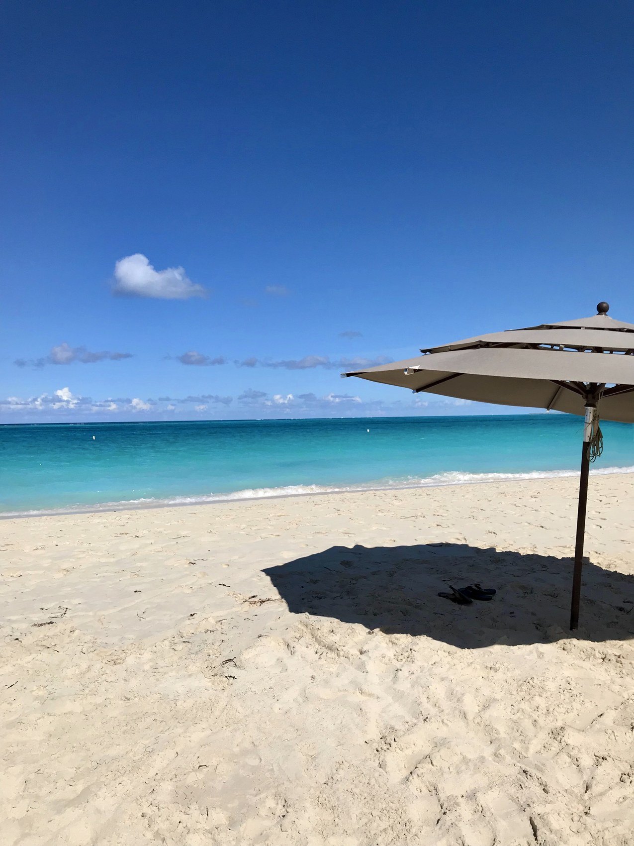 A single parasol on an empty white beach above turquoise water