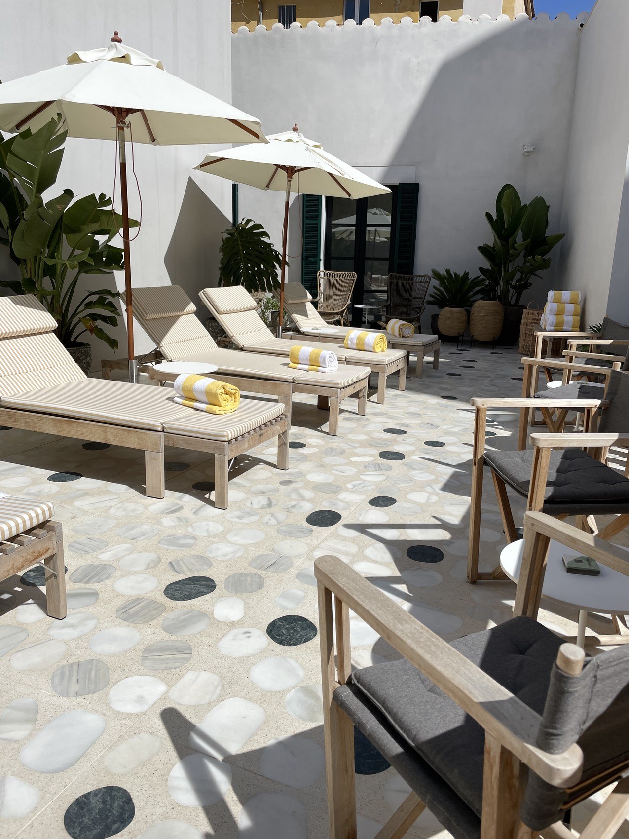 Loungers and parasols in a white walled courtyard on a pebbled terrazzo floor
