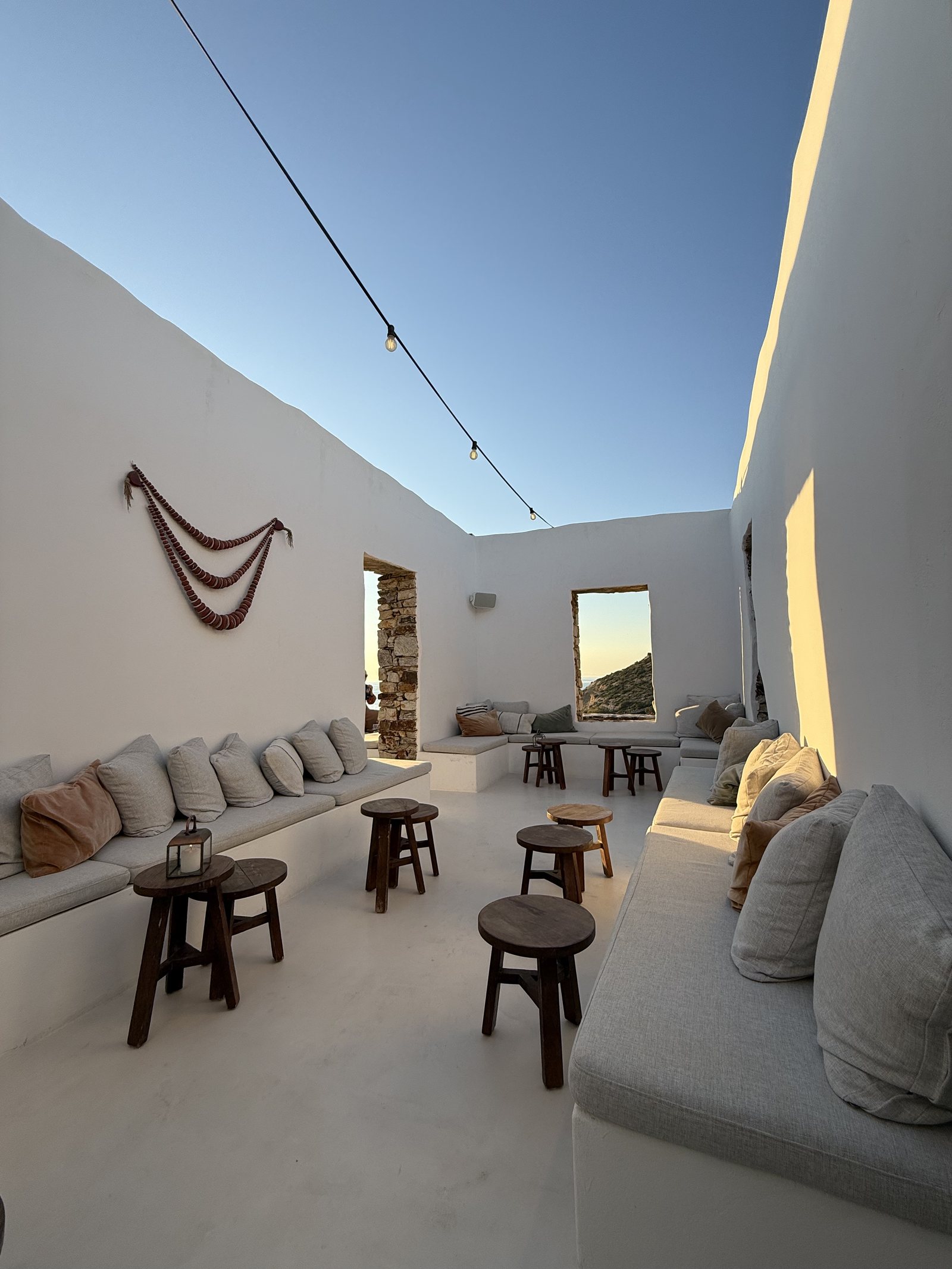 A white courtyard of built-in seating and low stools, open to the sea