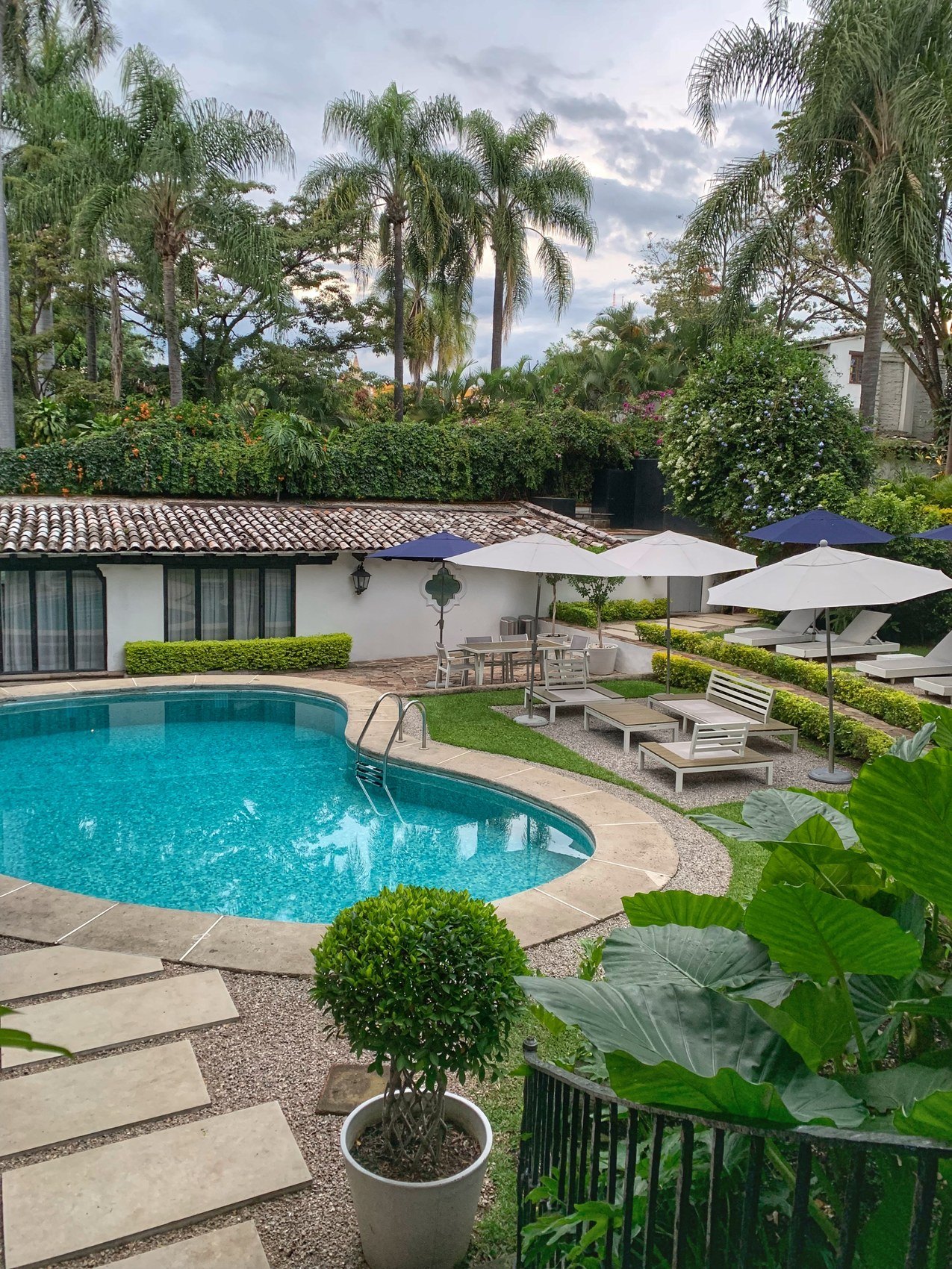 A tiled roof and white parasols above a pool in a palm garden