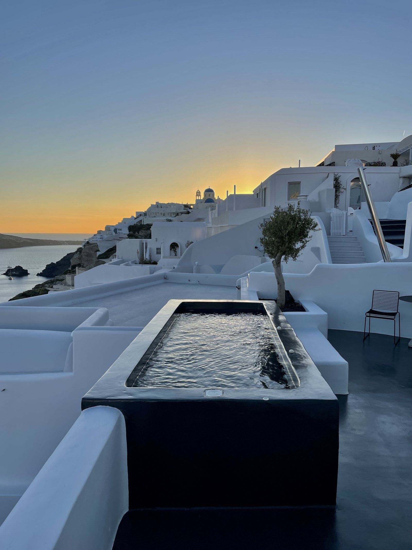 A white village at dusk above a terrace with a long plunge pool