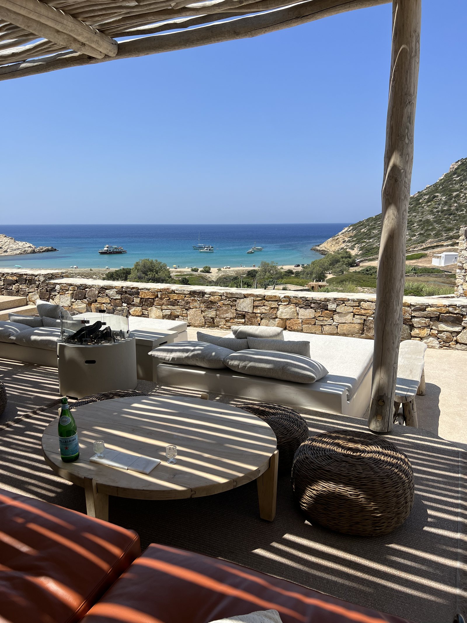 Daybeds and a low table on a terrace above a bay with boats at anchor