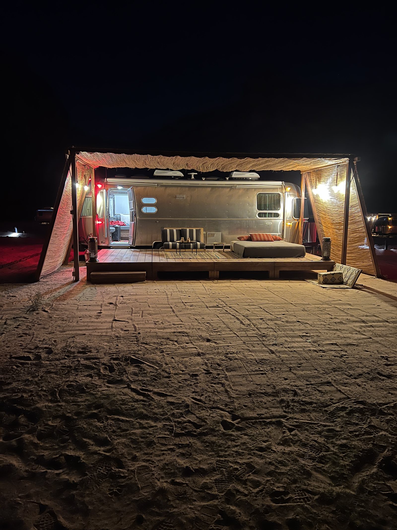 A lit Airstream standing open onto the sand in the desert at night
