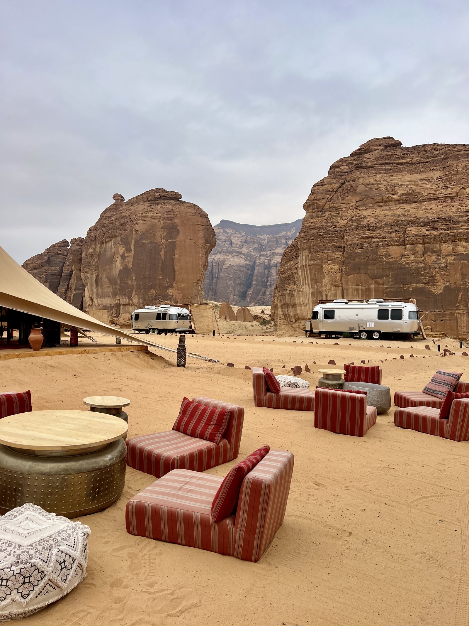 Low chairs set on the sand of a desert camp under the rock formations