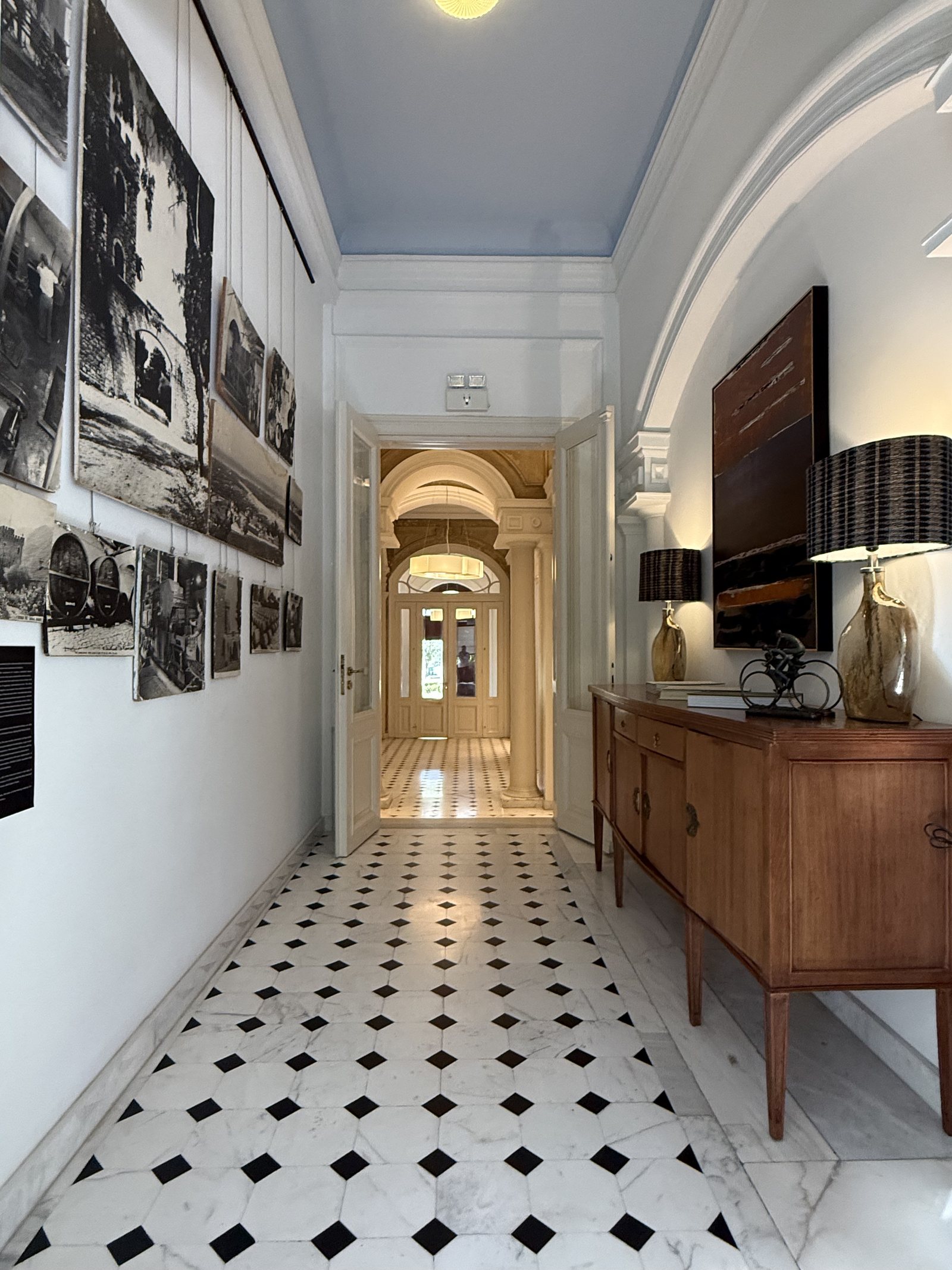 A corridor on a black and white diamond floor, photographs down one wall