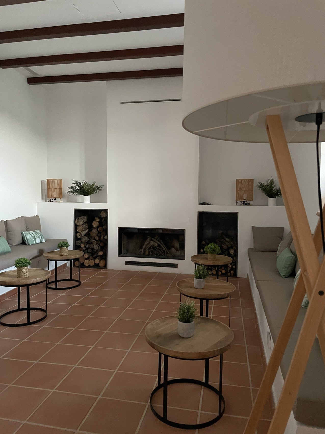 A sitting room with a built-in fireplace, stacked logs and low tables on a terracotta floor