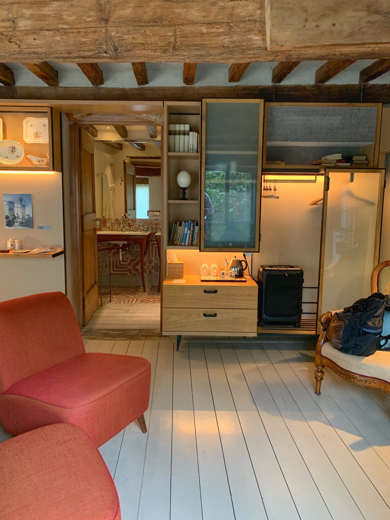 A pale boarded room with a red armchair, a timber dresser and a beamed ceiling