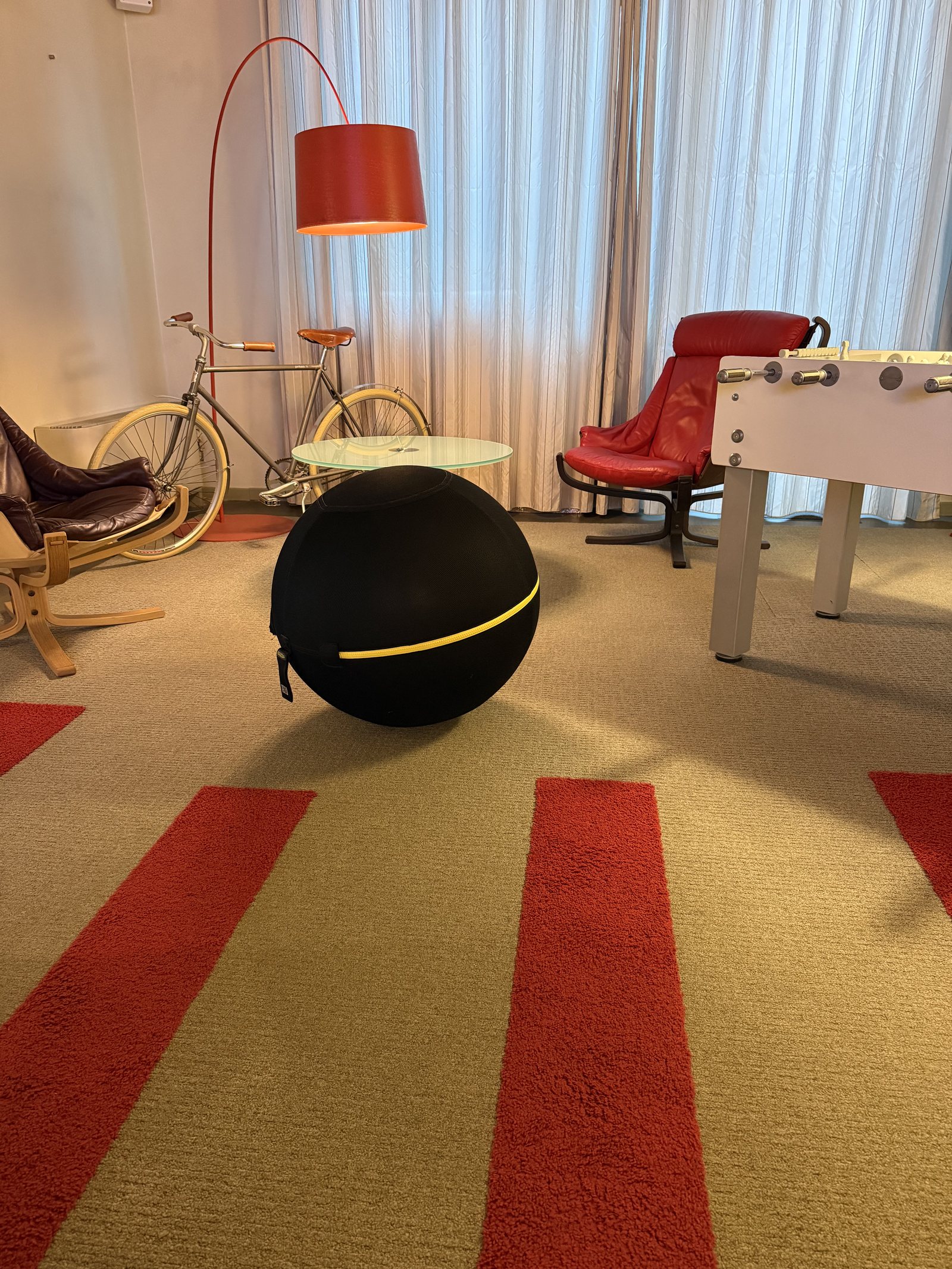 A table football beside a red arc lamp, a vintage bicycle and a striped carpet