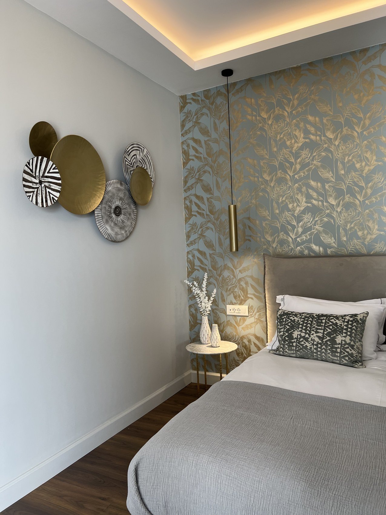 A bed against gold leaf wallpaper, ceramic discs hung on the wall beside it