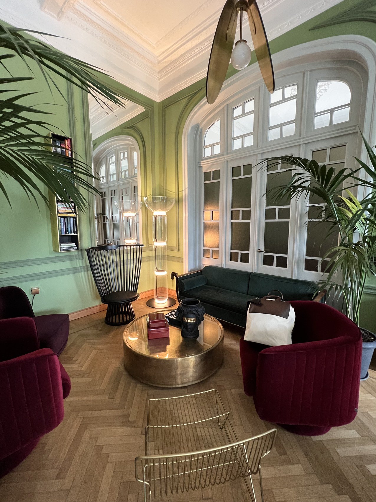A salon in pale green with arched windows, velvet chairs and palms