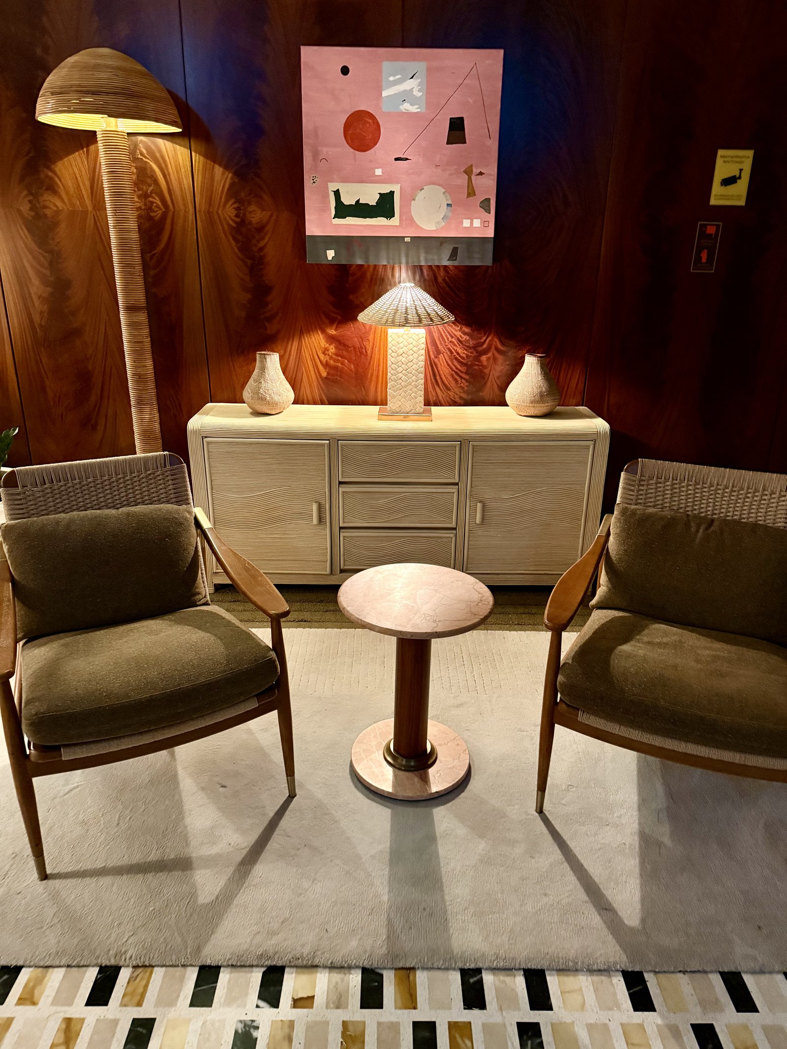 A pale sideboard and two low armchairs against a burgundy wall, with a shaded lamp and an abstract painting above