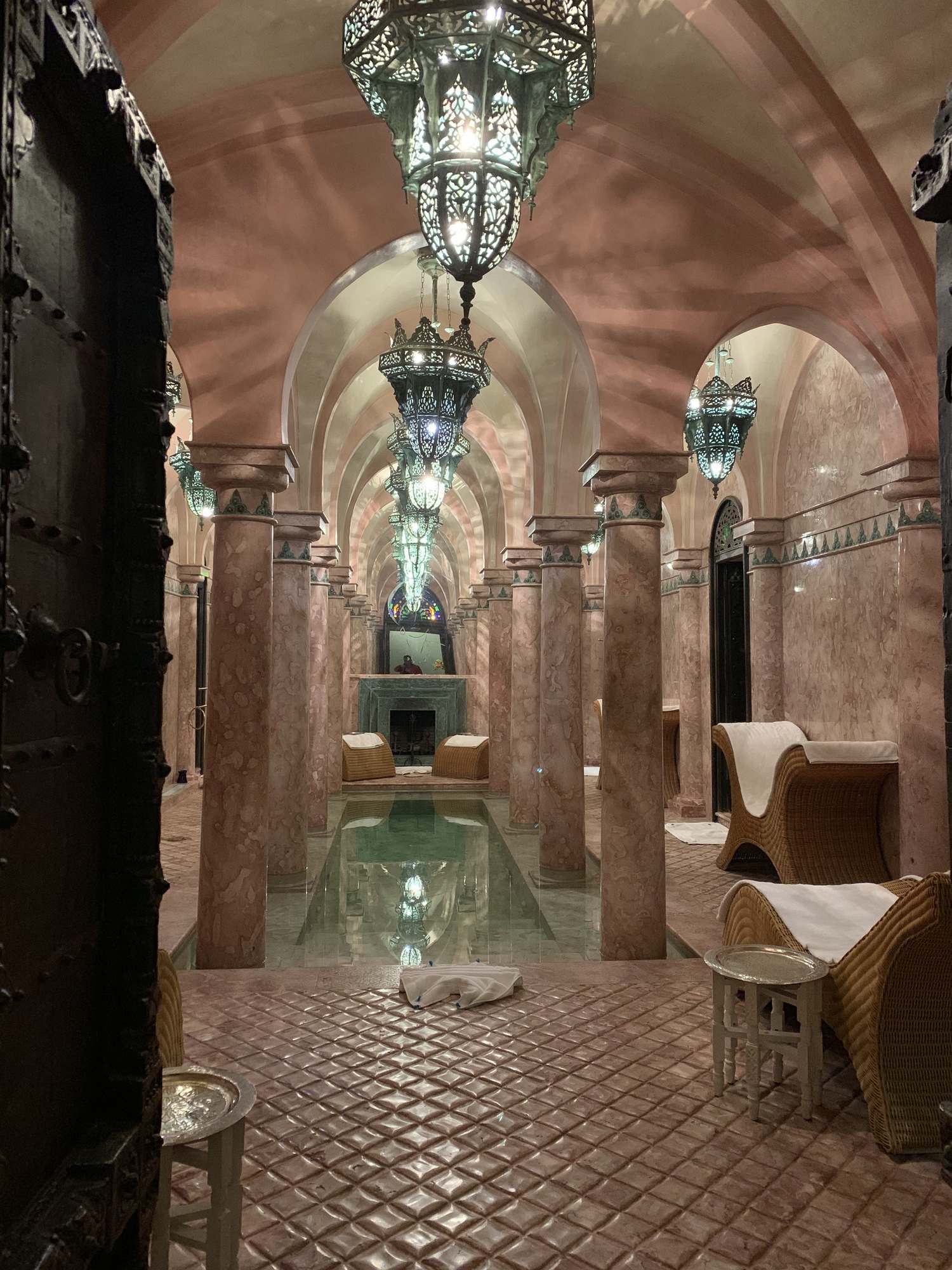 A narrow passage framed by heavy curtains, with a row of pierced metal lanterns hanging down it above a carved timber door
