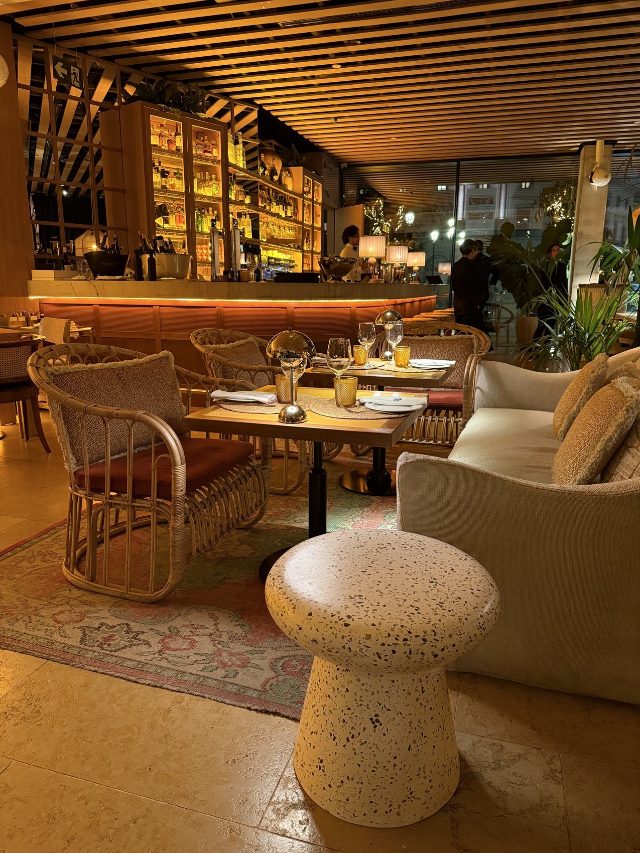 A bar and restaurant under a slatted timber ceiling, with cane chairs and a stone stool
