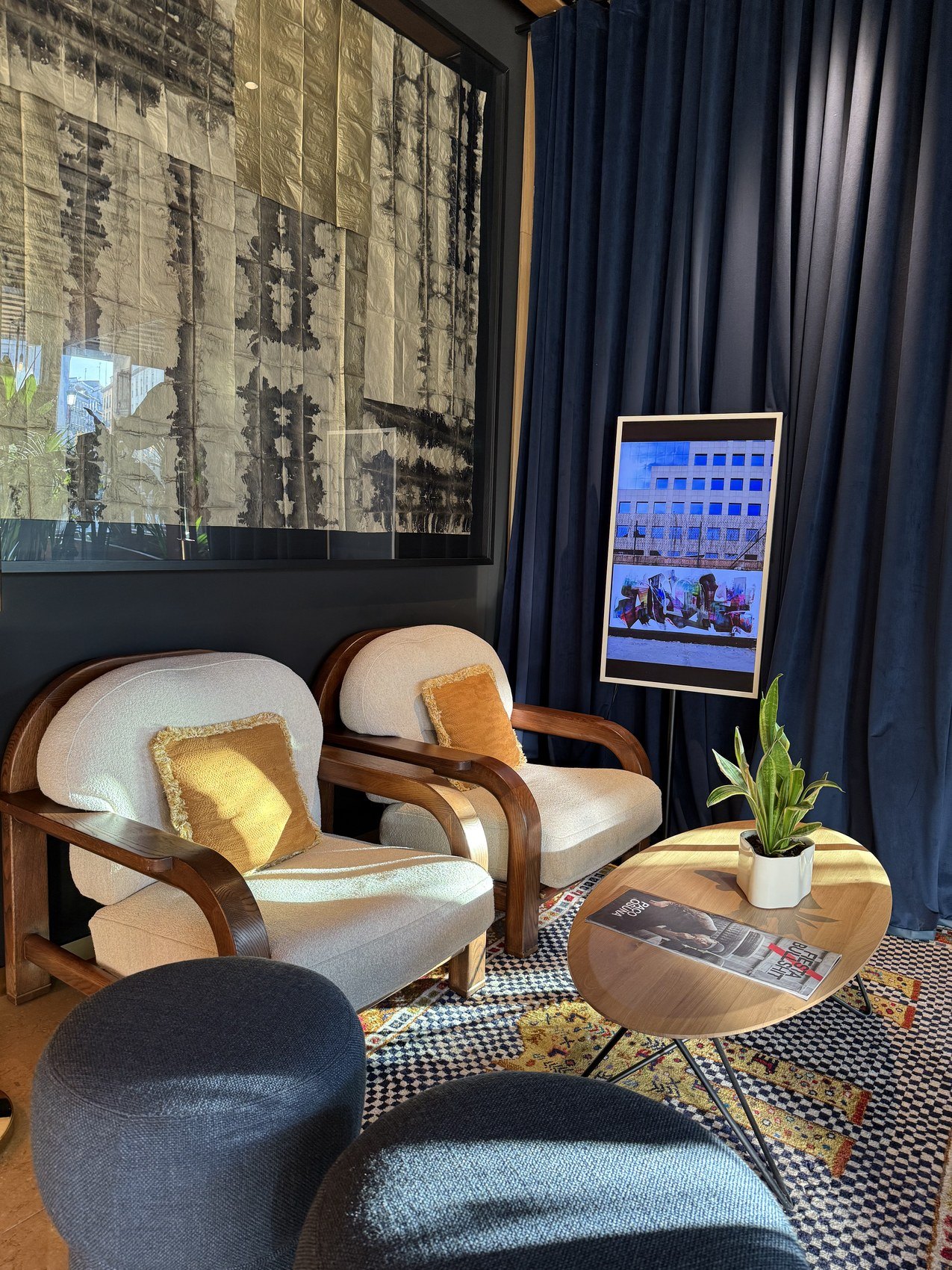 Pale armchairs and a round table in a hotel lounge against a printed wall and a blue curtain