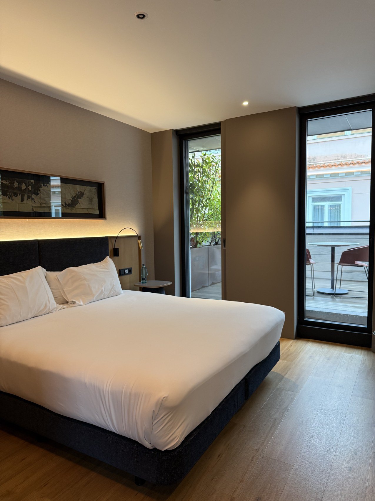 A bed in a pale room with the balcony doors open onto the street