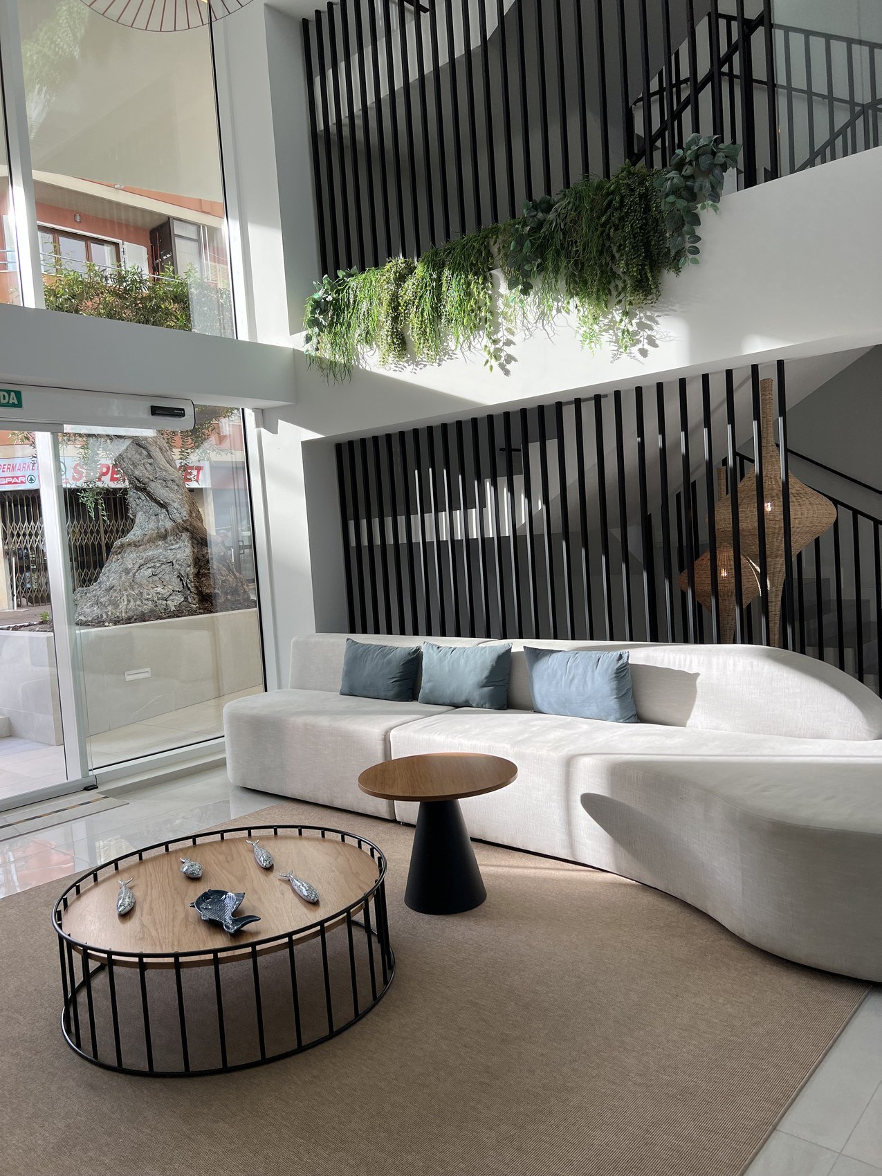 A long curved white sofa in a double height lobby behind a slatted black screen hung with ferns