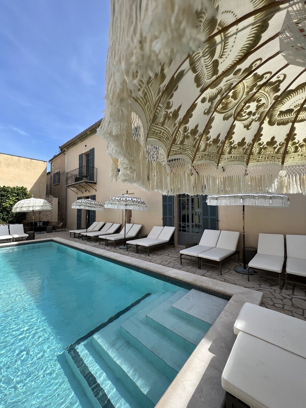 A pool below a scalloped canopy, loungers and parasols along the far side