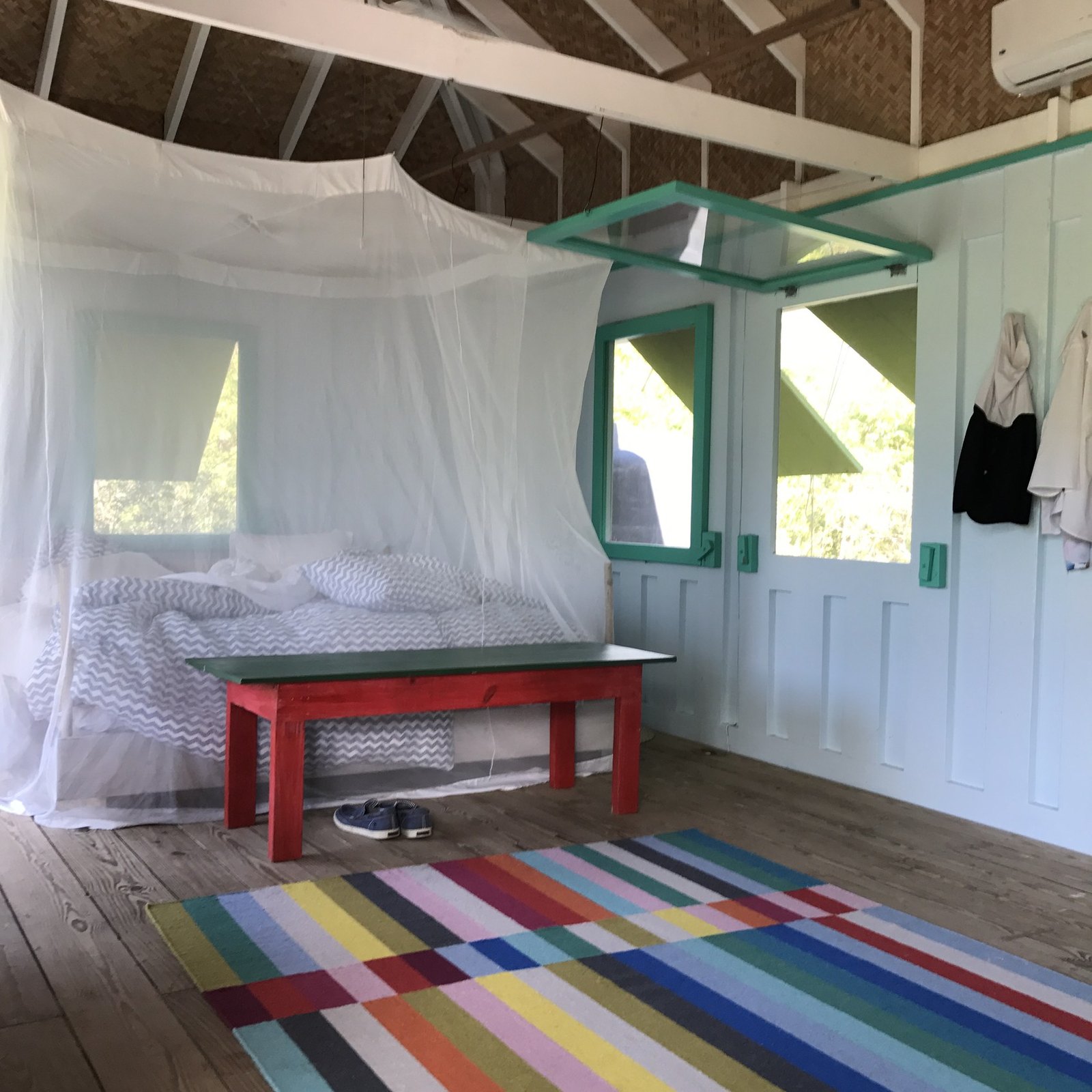 A bed under a mosquito net in a timber cabin, a striped rug on the floor