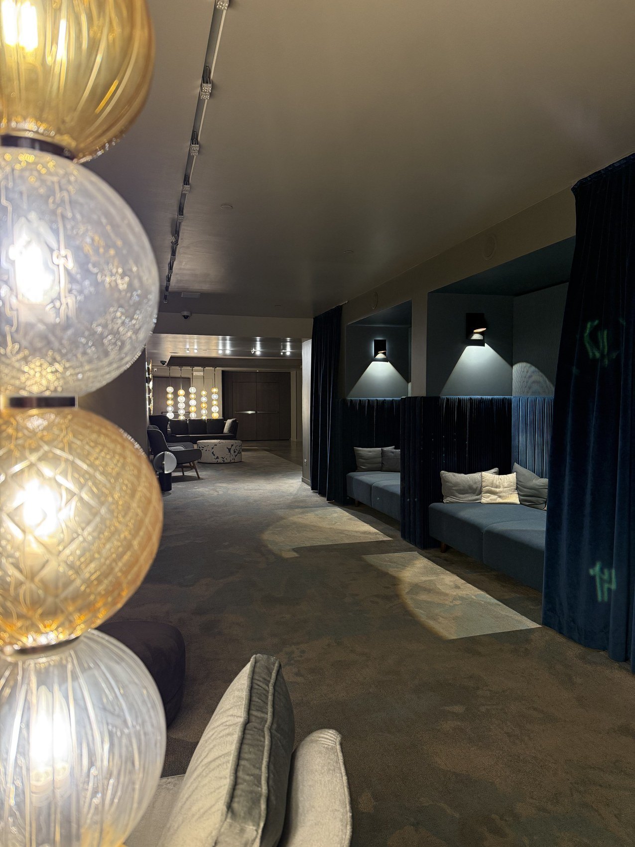 Amber Murano glass globes hanging in a row over a dark lounge with blue alcoves beyond