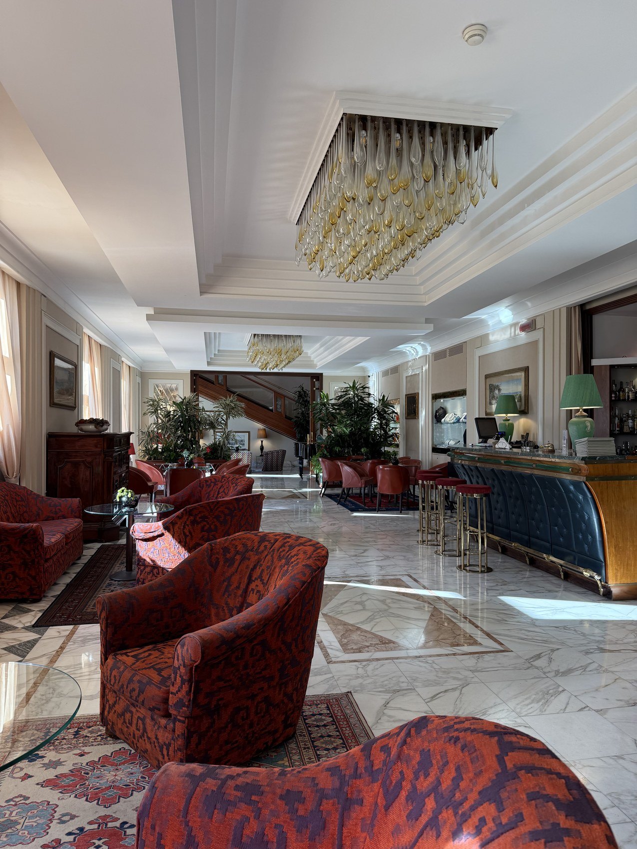 A long lobby with red velvet armchairs and a glass chandelier on a marble floor