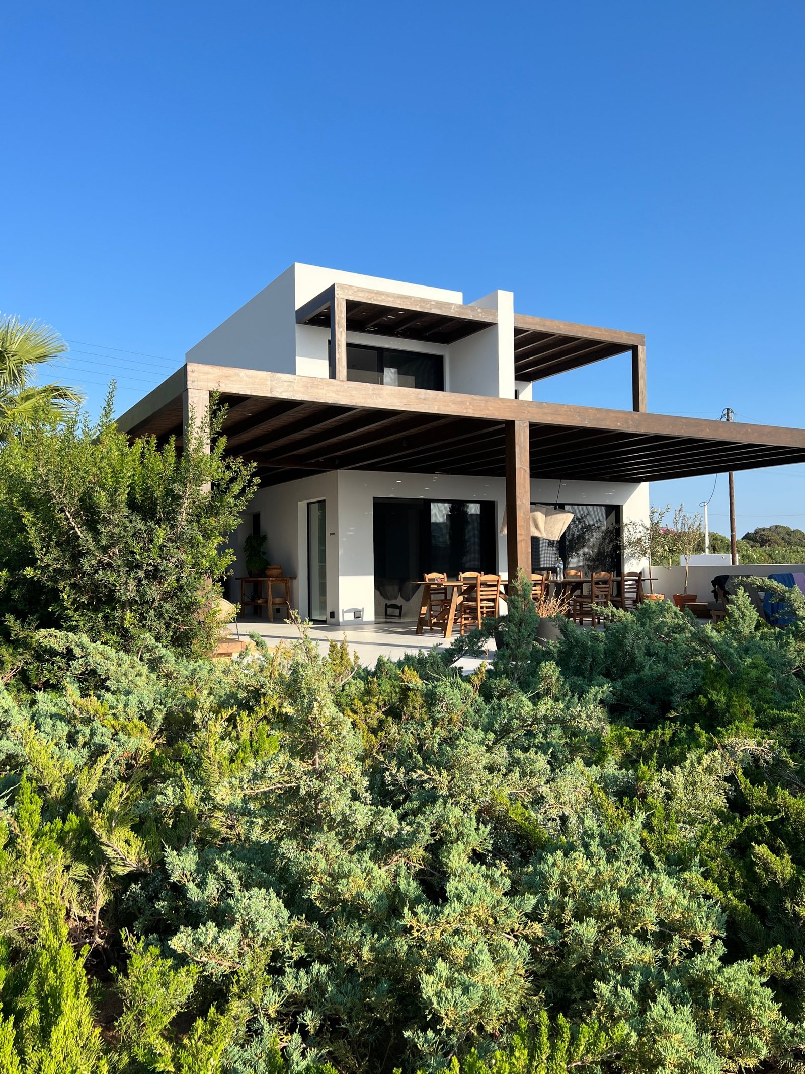 A white house under deep timber pergolas, junipers in front of it