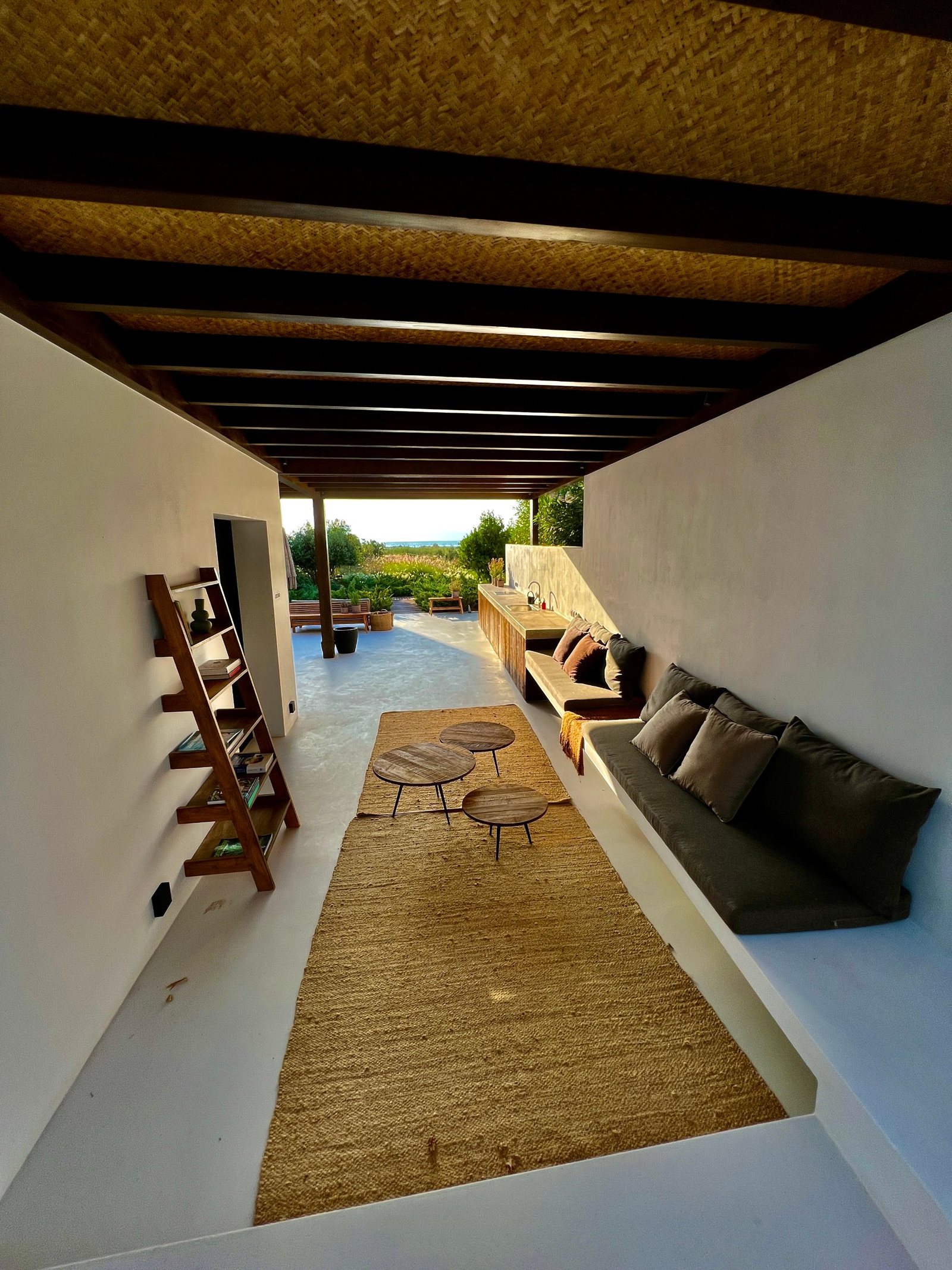 A long outdoor lounge under a cane ceiling, opening to the sea