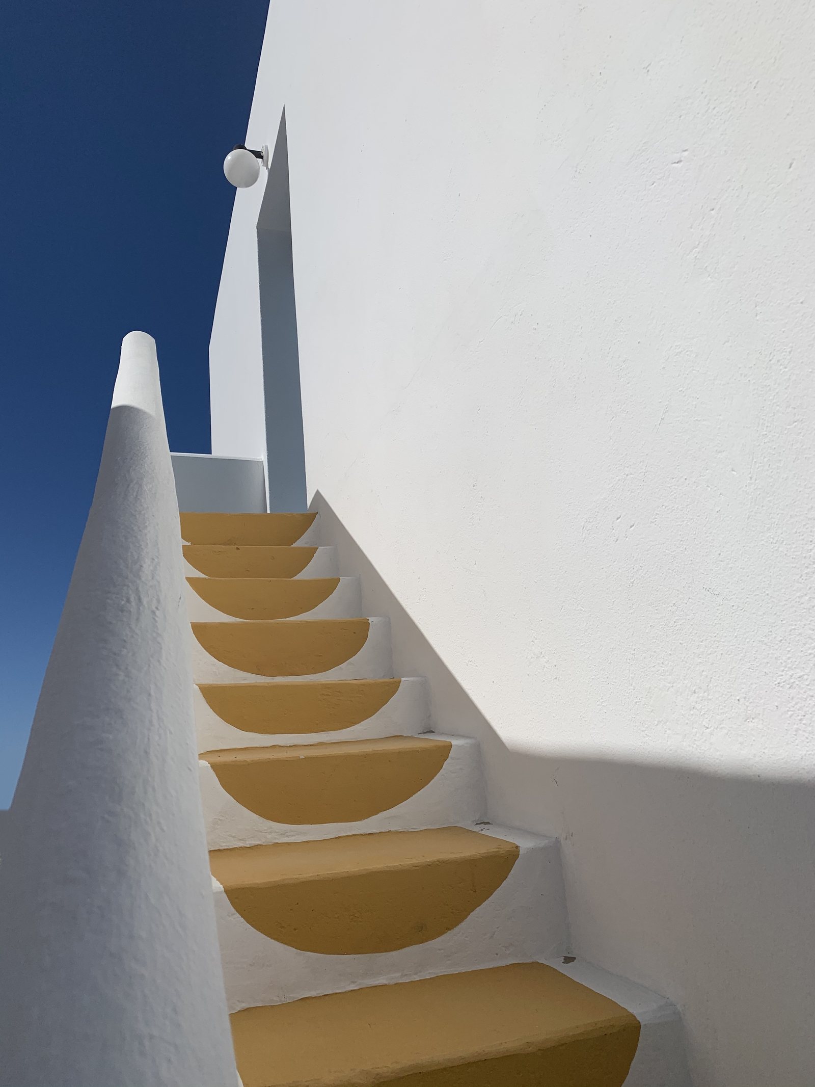 Ochre steps climbing a white wall against a deep blue sky