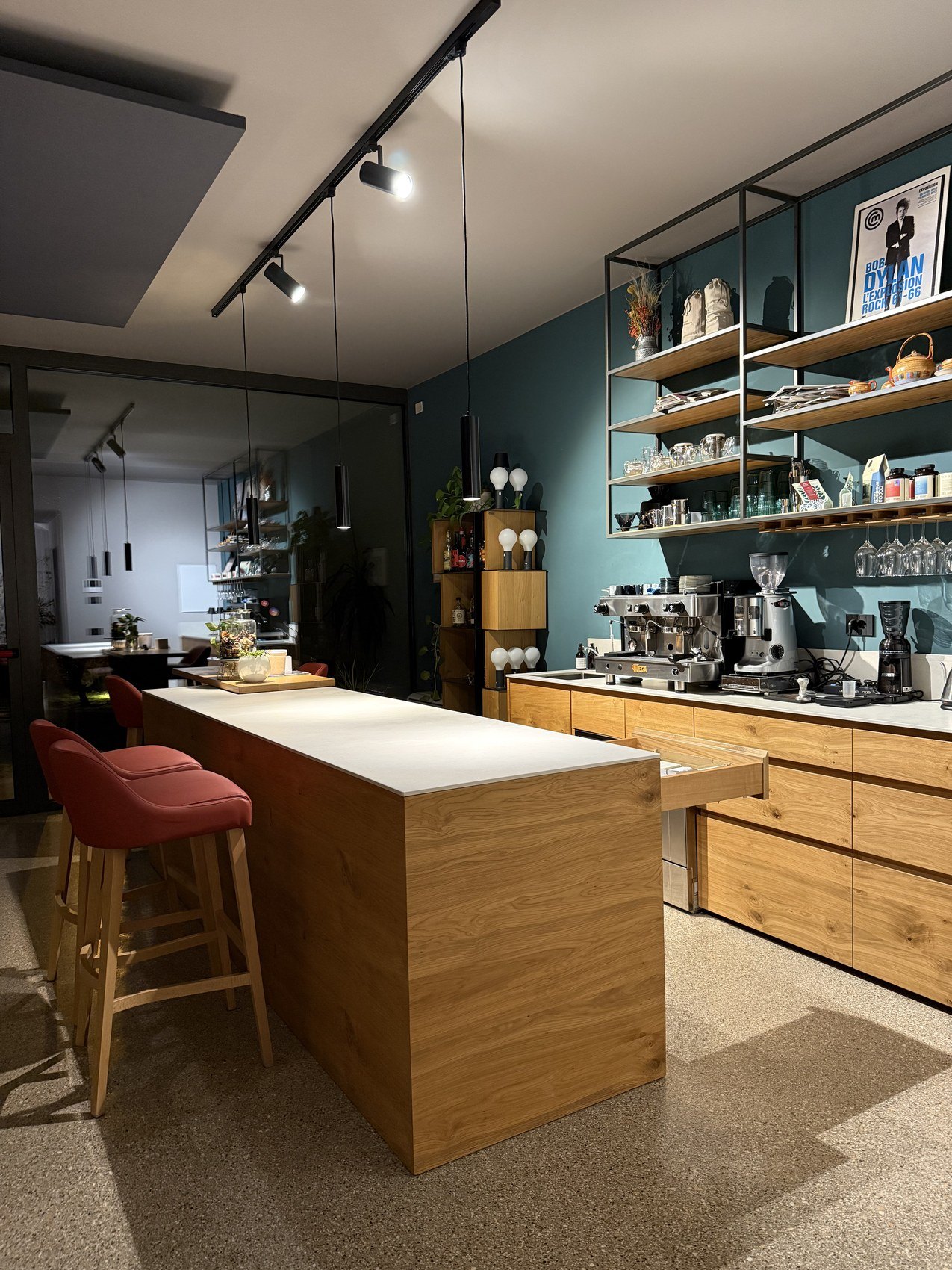 An open kitchen with a timber island, red stools and teal shelving stacked with glassware