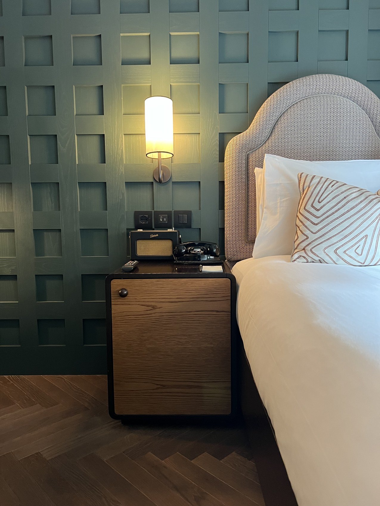 A bed with an arched pale headboard against a panelled dark green wall