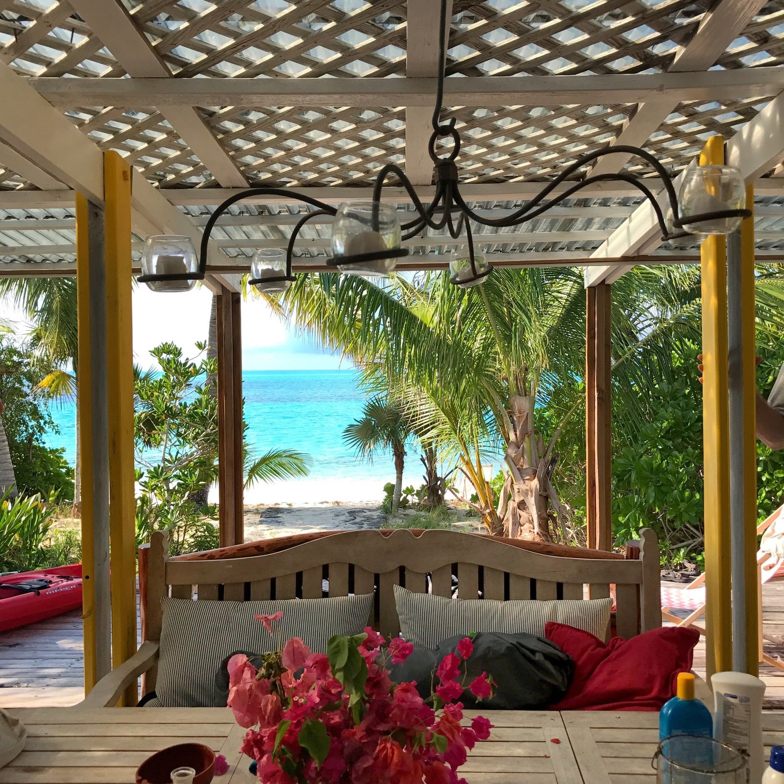 A wooden daybed with red cushions under a lattice pergola, the sea beyond the palms