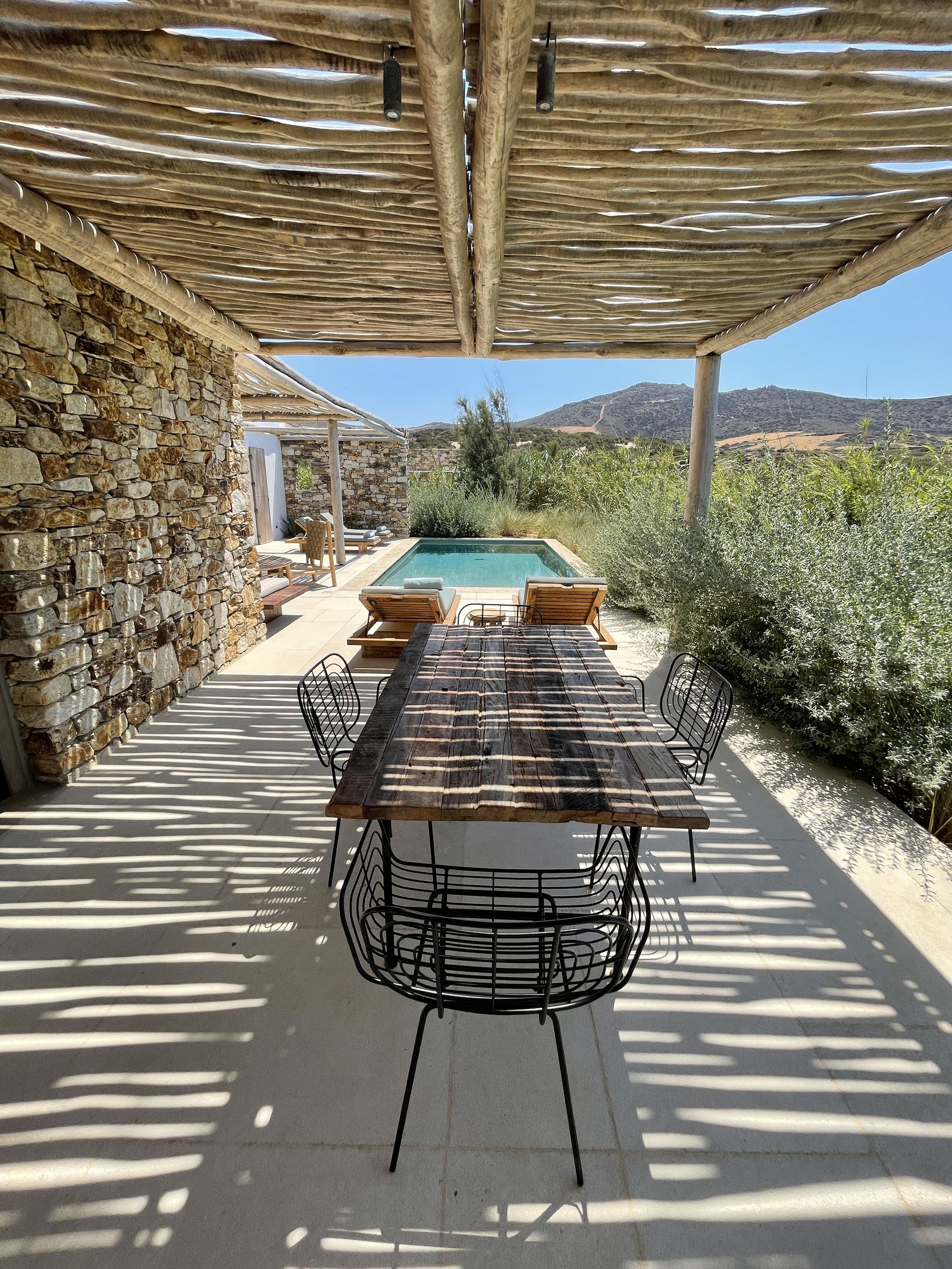 A long table under a bamboo pergola against a dry stone wall