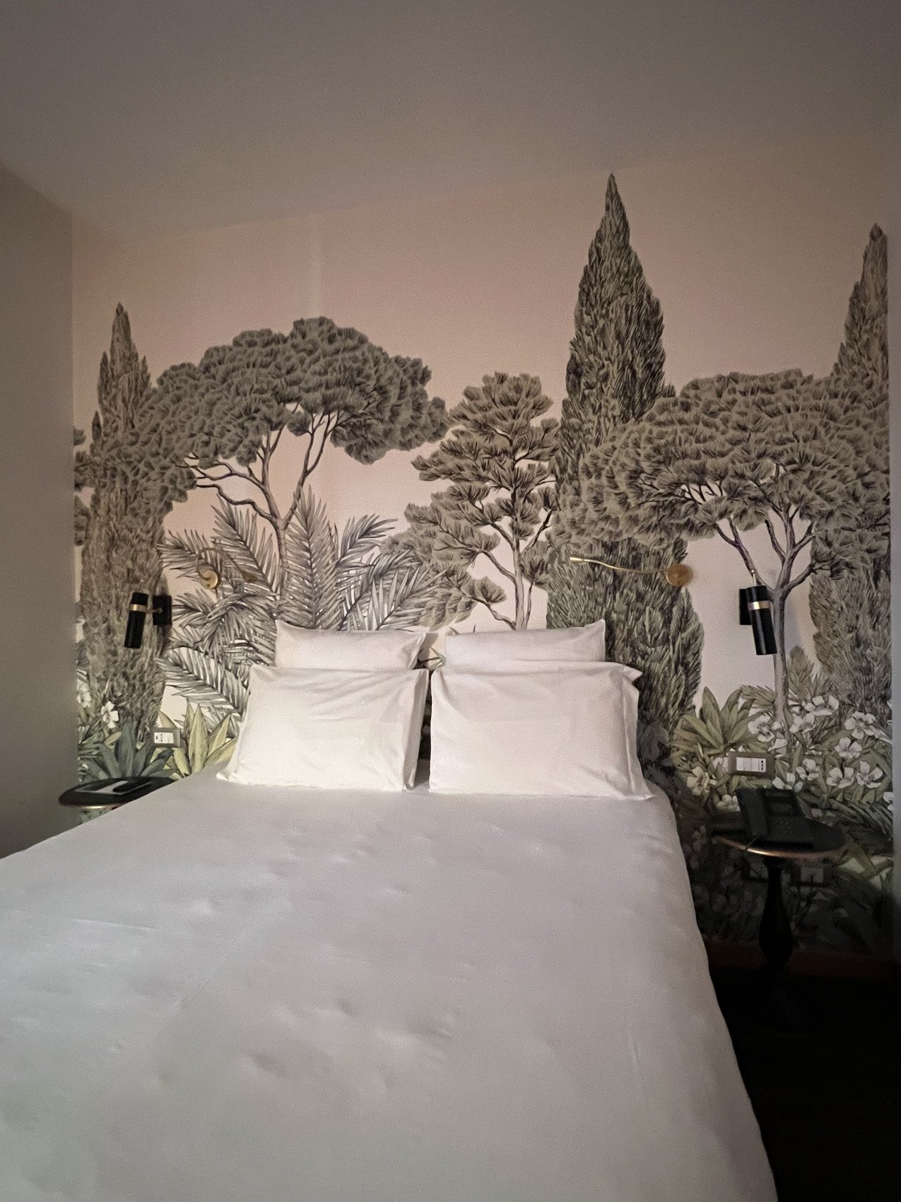 A bed against a wall painted with umbrella pines and cypresses