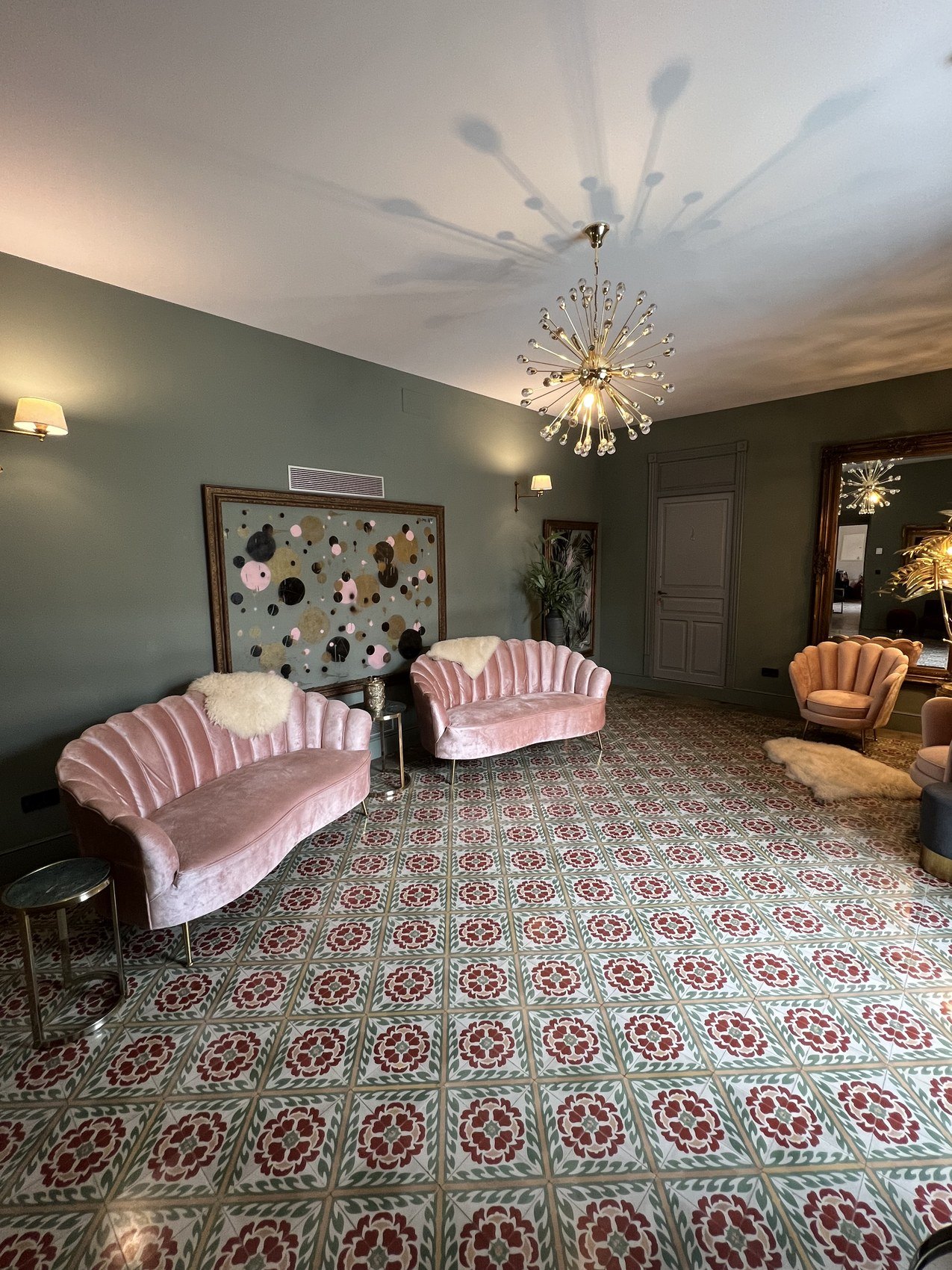 A pale green salon with two pink velvet sofas on a red and green patterned tile floor