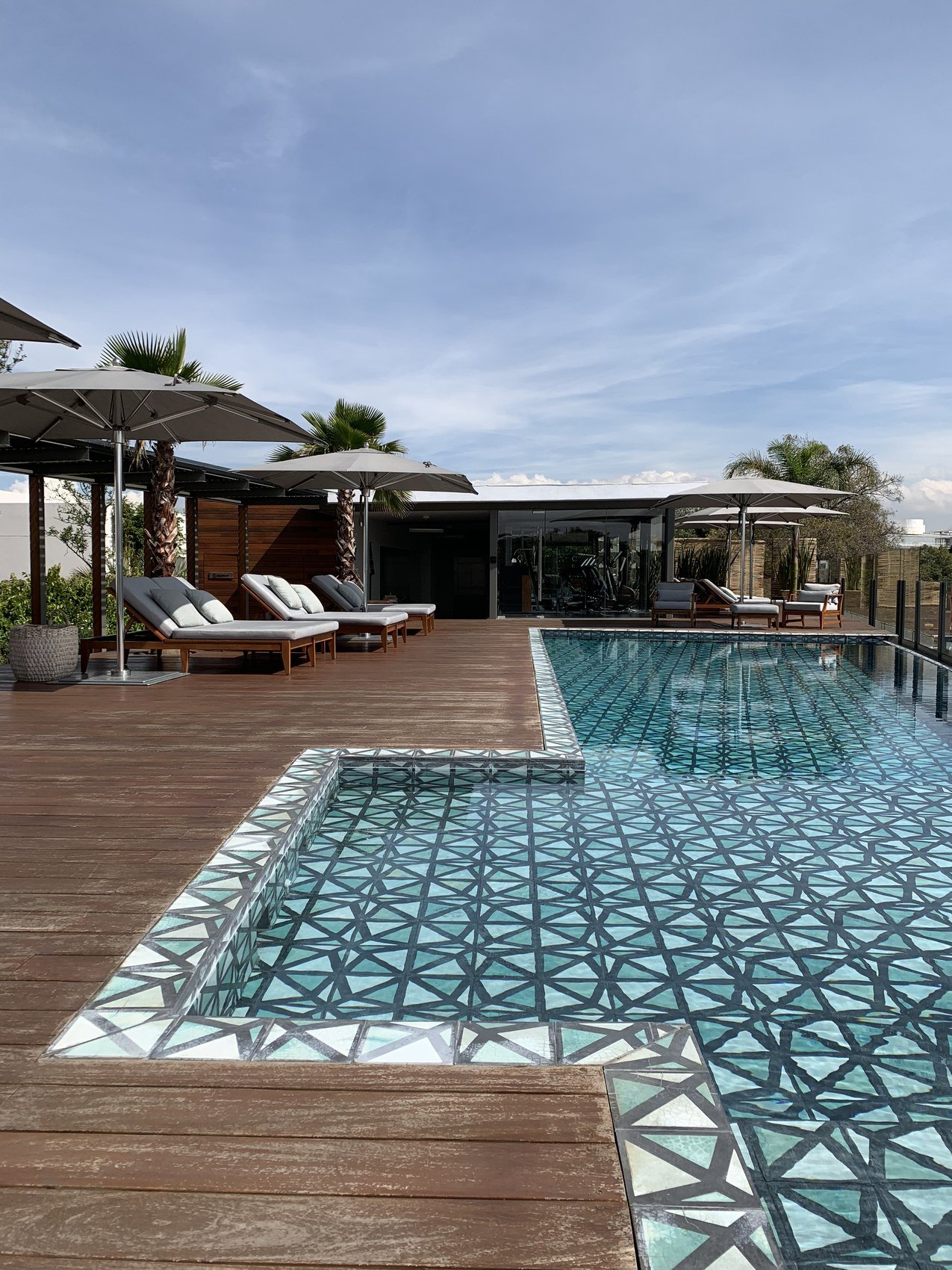 A pool tiled in a green geometric pattern, teak decking around it