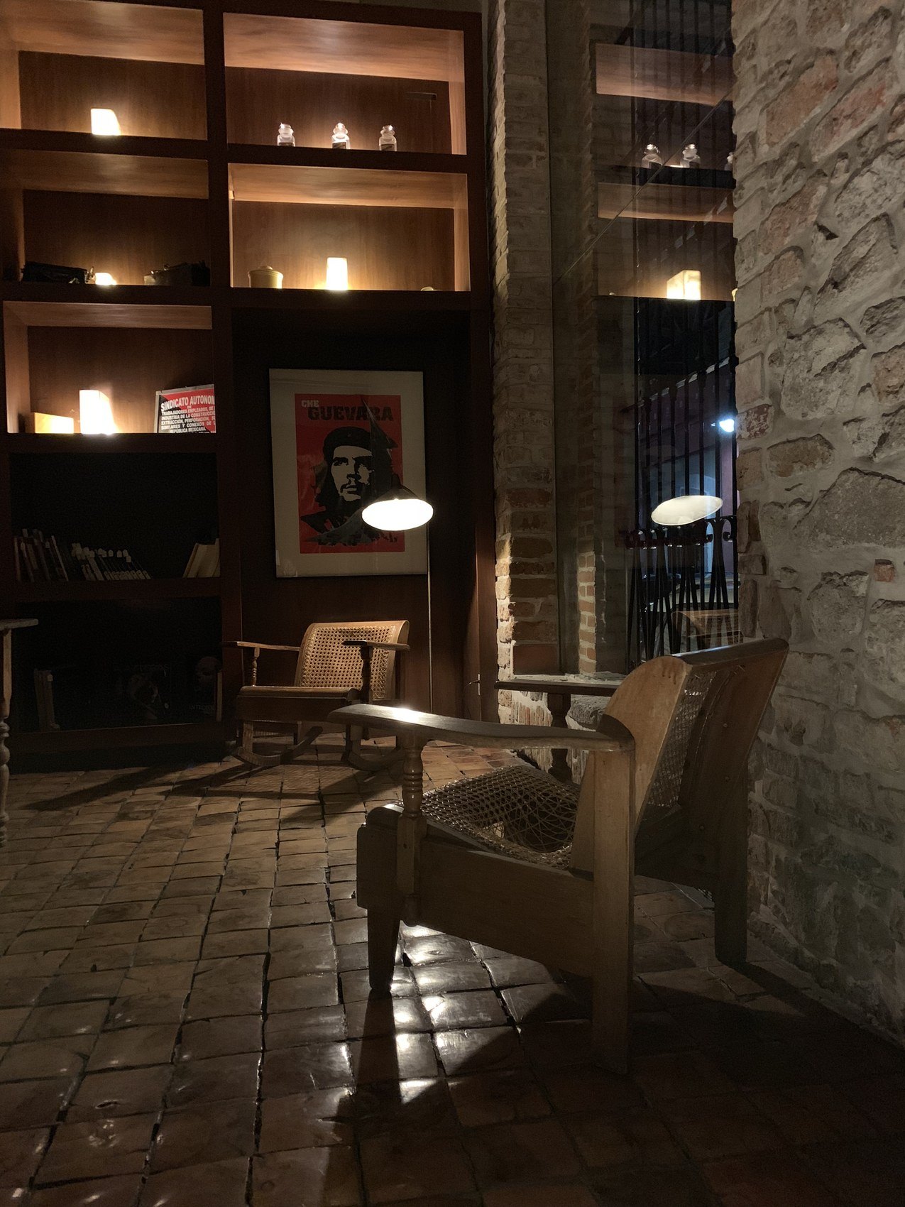 A dark library corner of stone and timber shelves, two cane armchairs under the lamps