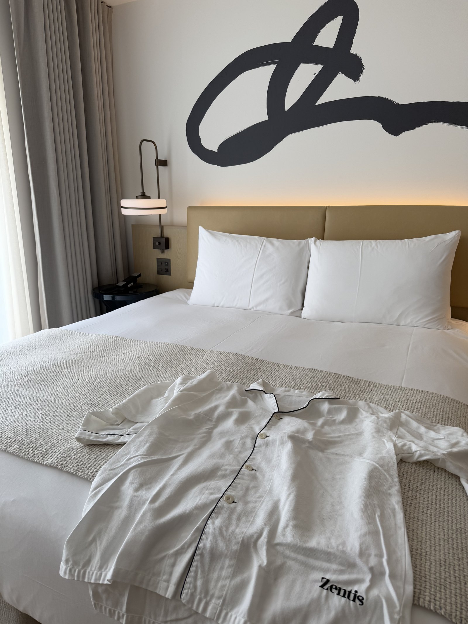 White pyjamas laid out on a made bed beneath a large black calligraphic mark on the wall