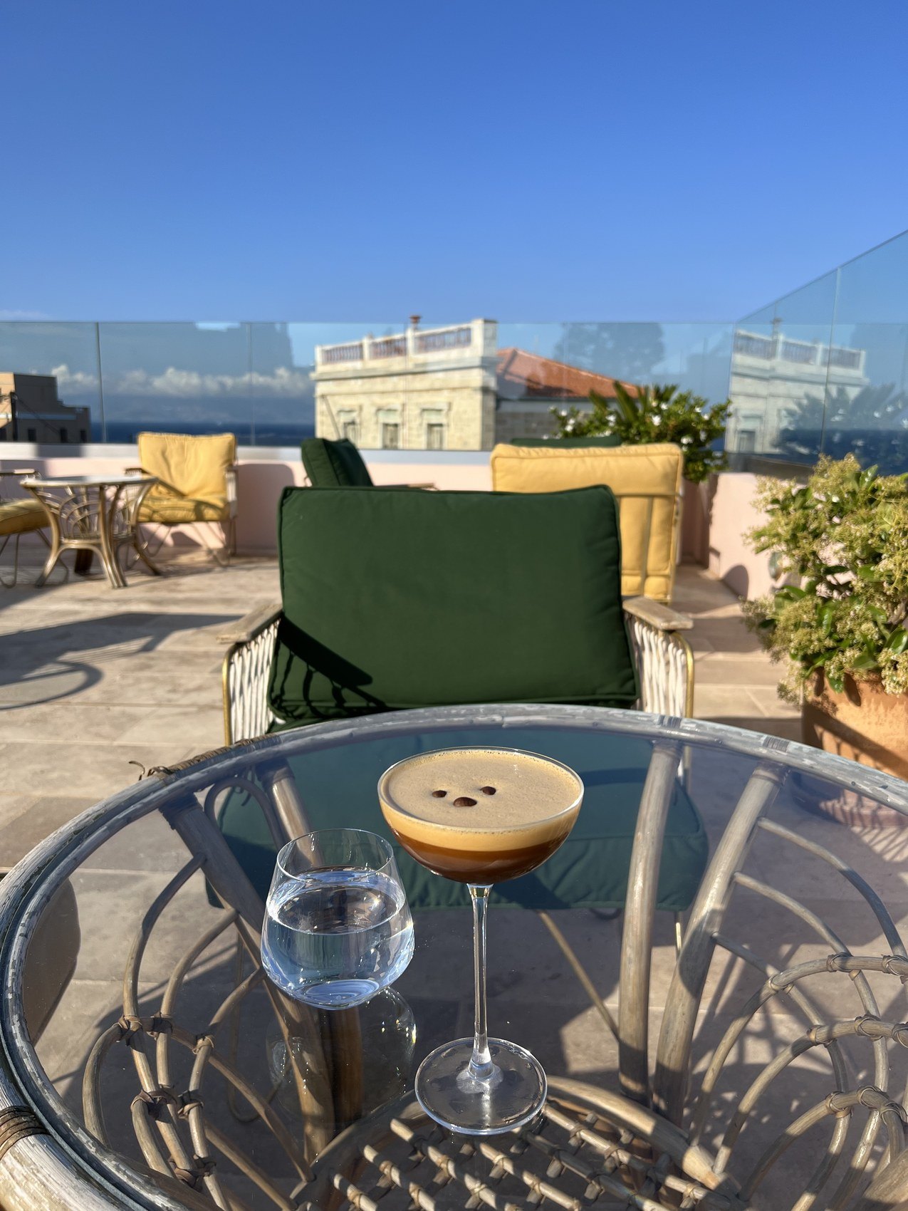 An espresso martini and a glass of water on a glass table on a roof terrace