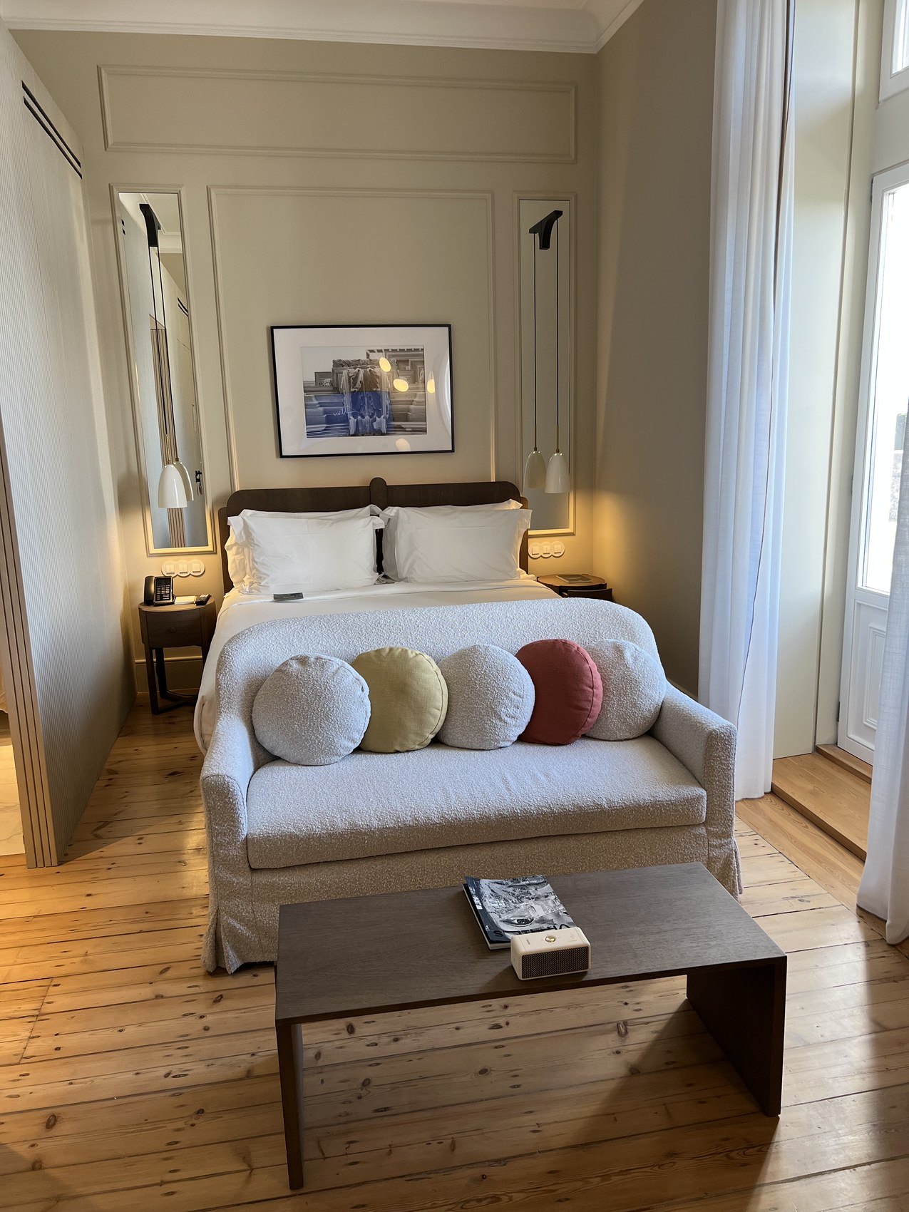 A pale sofa with a row of round cushions at the foot of a bed on a bare timber floor