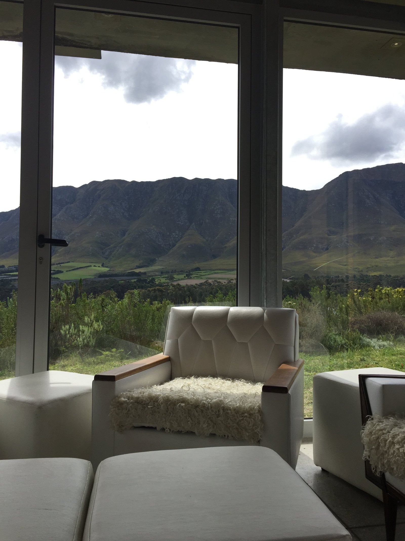 A white leather armchair with a sheepskin on the seat, in front of floor-to-ceiling glass looking out to green farmland and a long mountain ridge