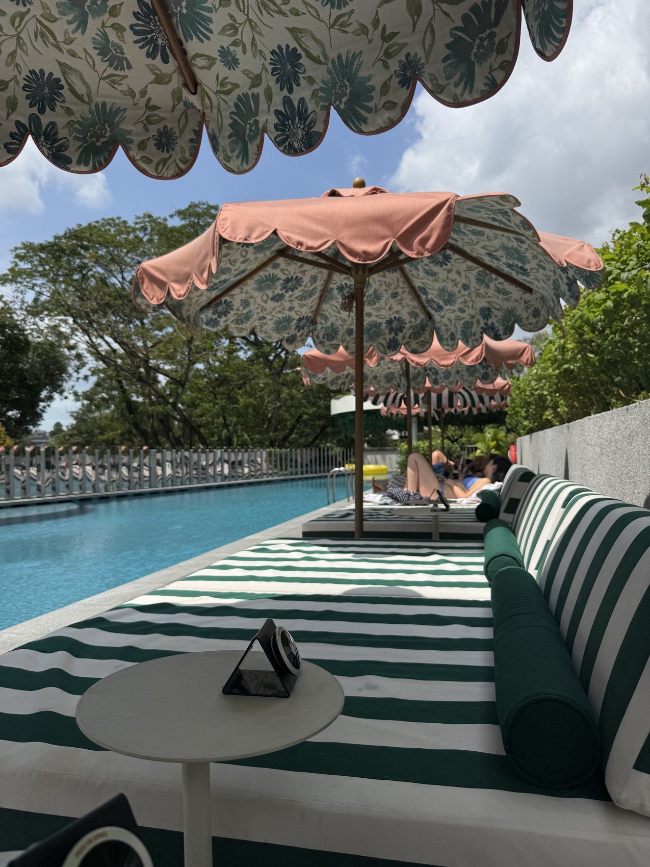 Striped loungers and pink parasols along a rooftop pool under a scalloped awning
