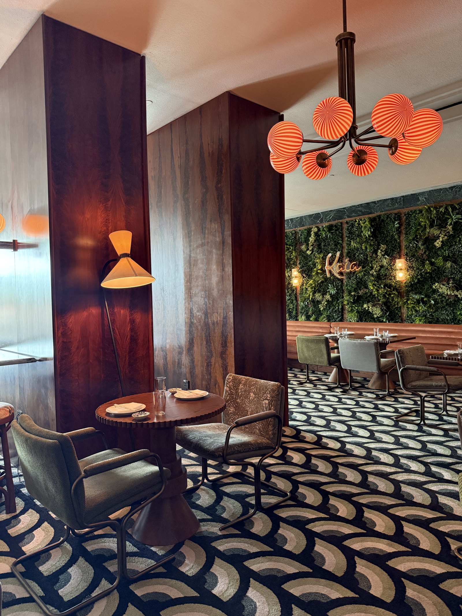 A corner table and leather chairs beside a tall rosewood screen, under a chandelier of striped orange glass globes