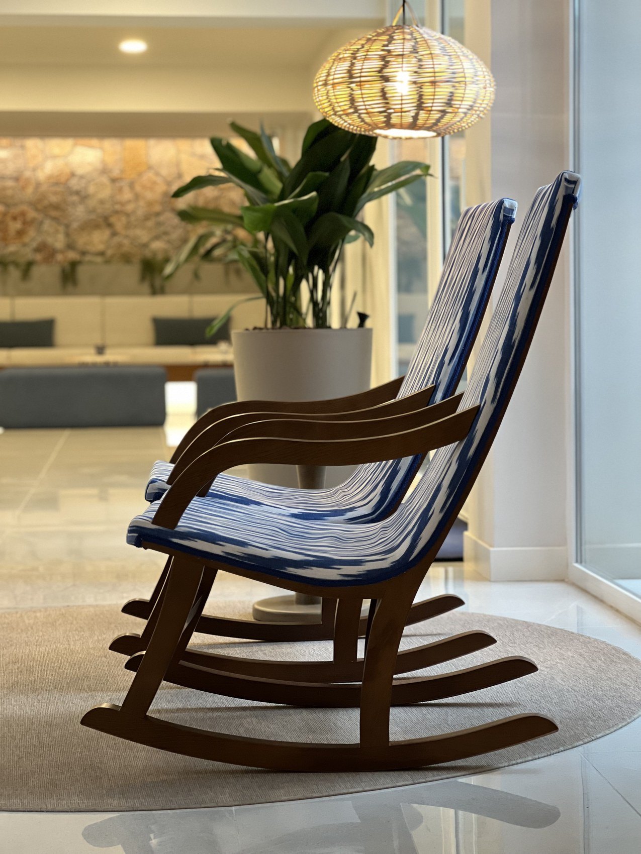 A timber rocking chair in blue and white stripes on a round rug under a woven globe lamp