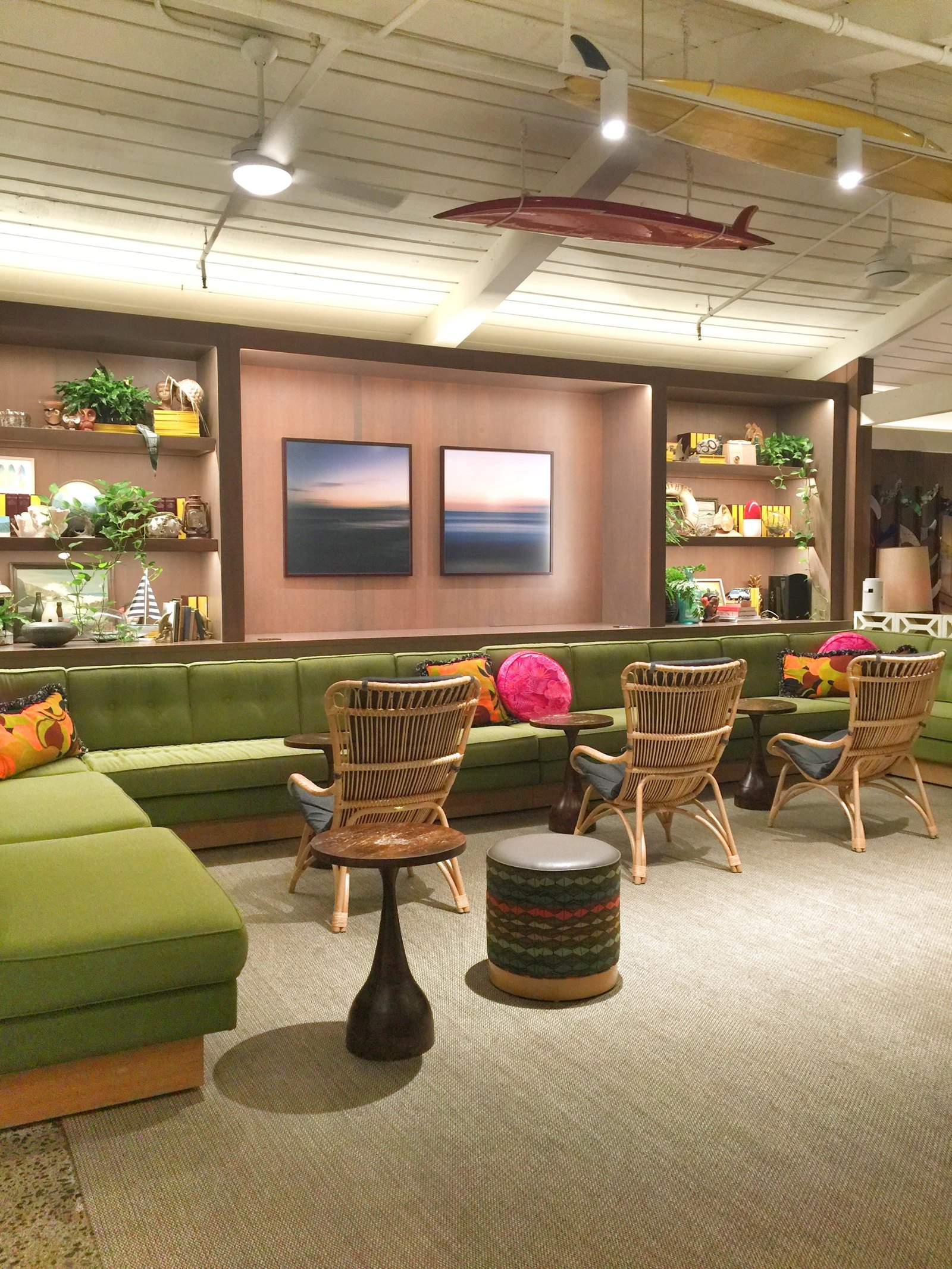 A lounge with surfboards slung from the white boarded ceiling, long green banquettes and rattan armchairs
