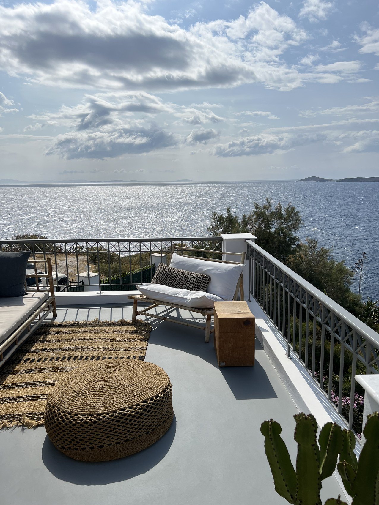 A terrace above the water with a daybed, a woven pouf and a cactus in the corner