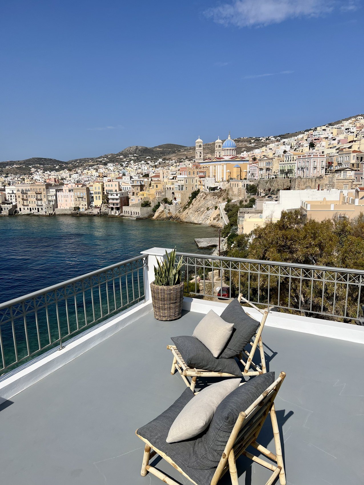 Two bamboo loungers on a terrace, the town climbing the hill across the water