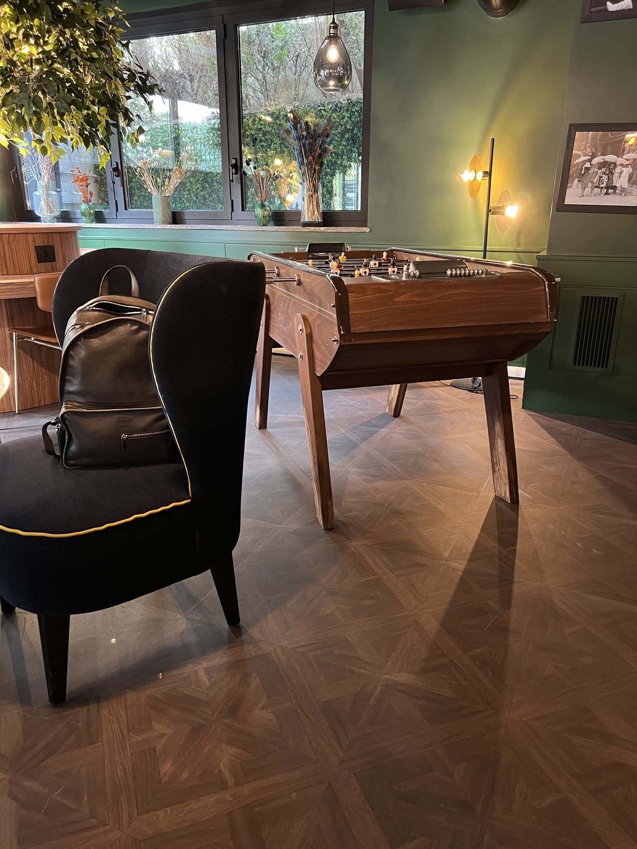 A timber table football on a parquet floor beside a dark armchair, a garden through the window