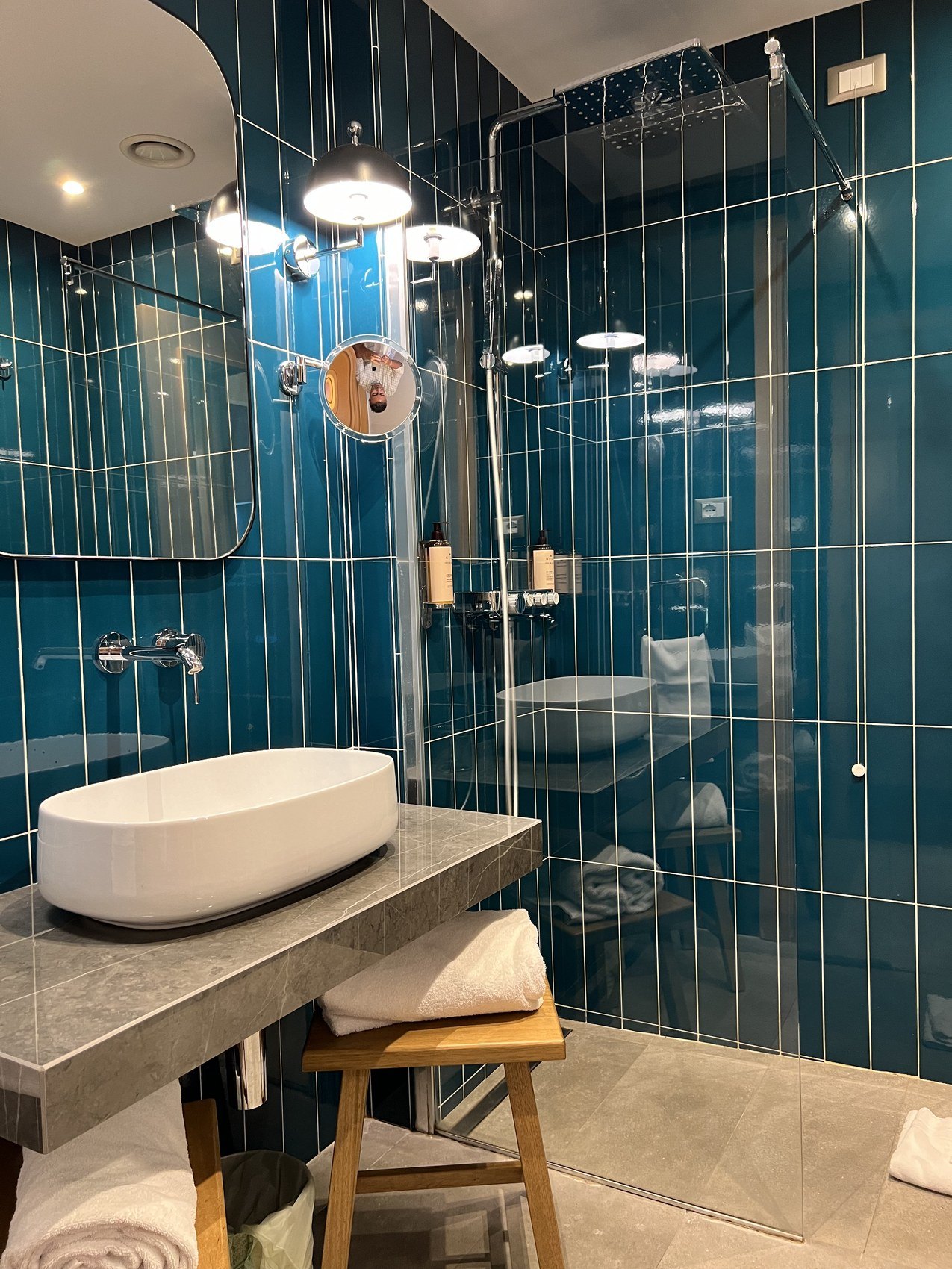 A shower room tiled in teal with a stone basin and a timber stool