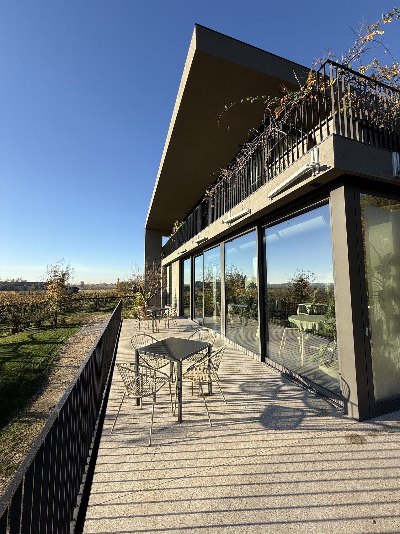 A long terrace of a dark modern building with metal tables, overlooking open fields