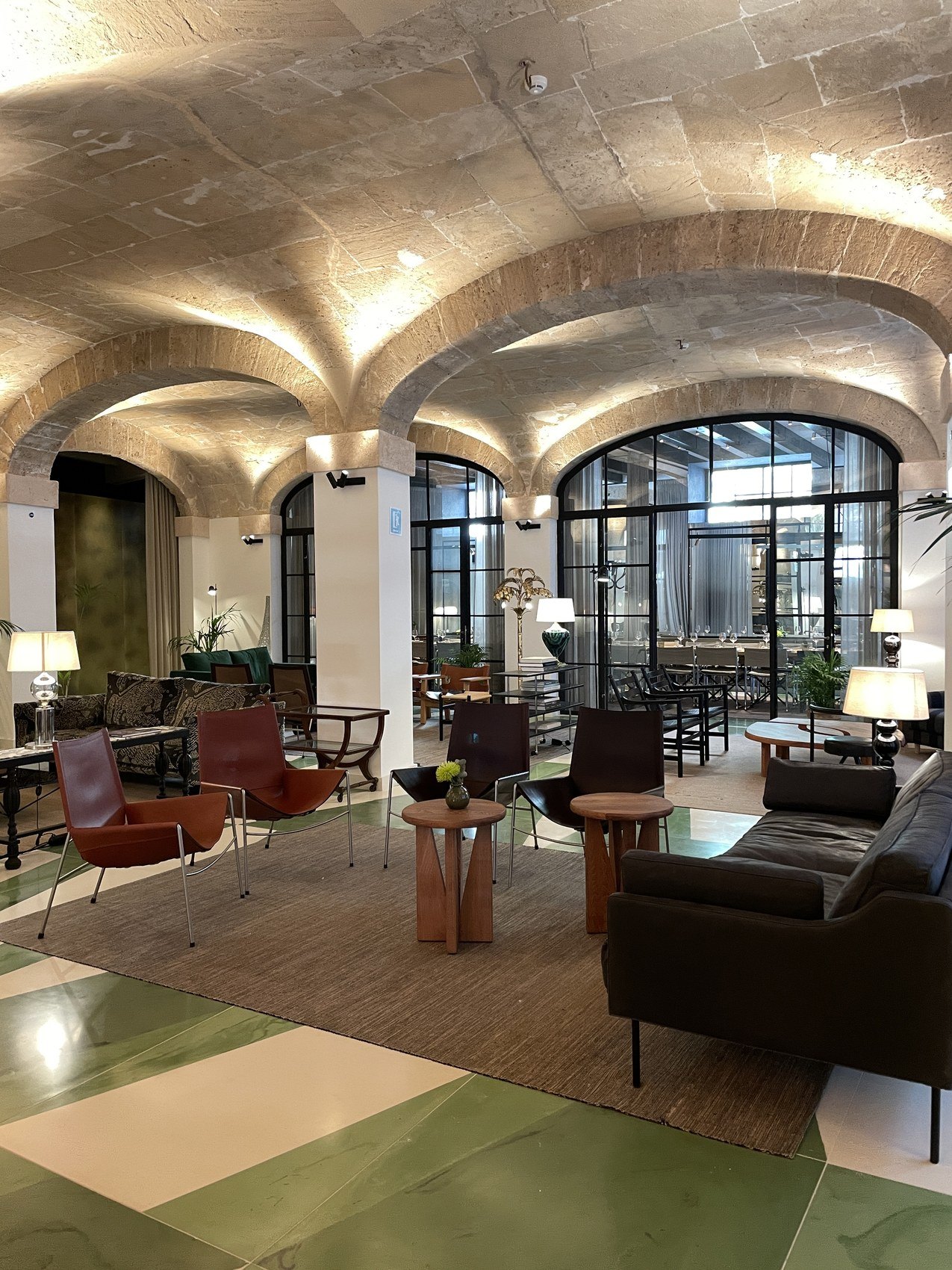A vaulted stone lounge with leather chairs and low tables on a green painted floor