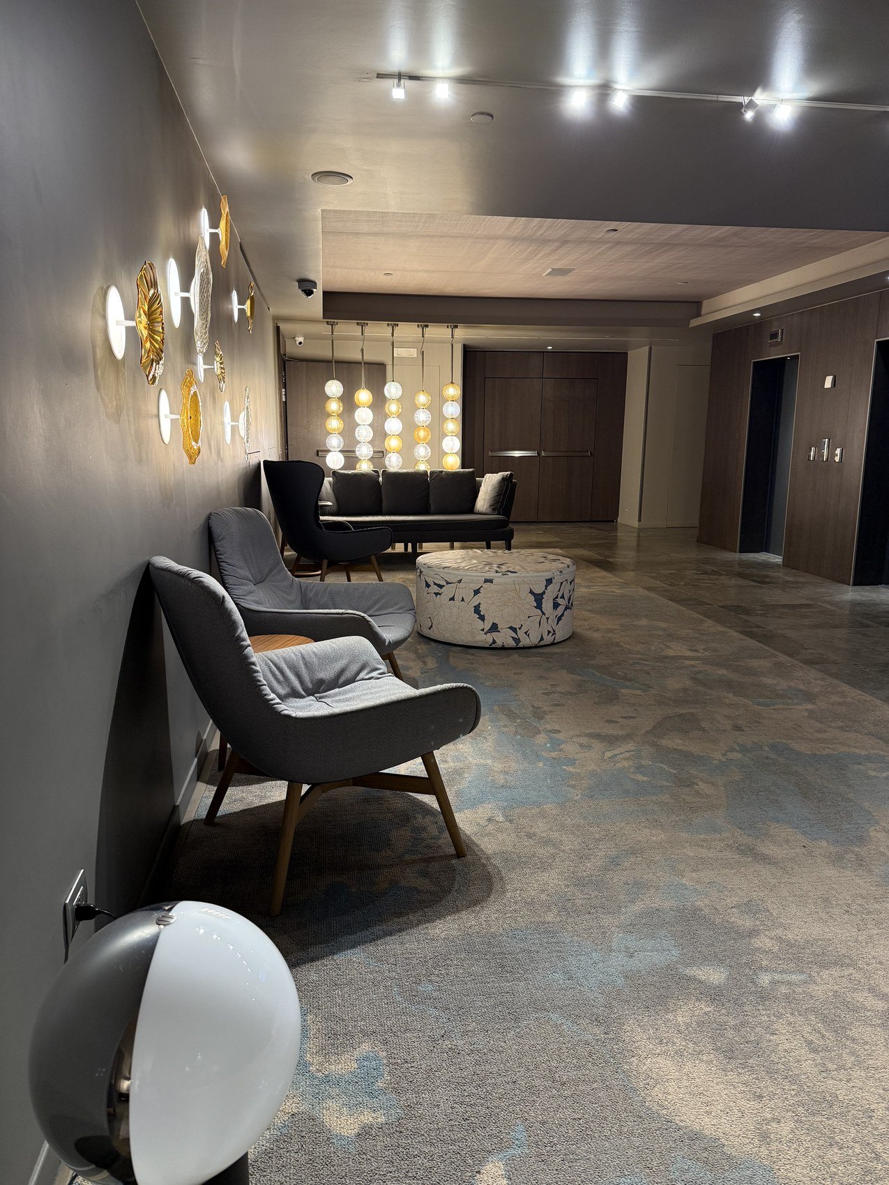 A lobby with sculptural wall lights, low chairs and a patterned carpet